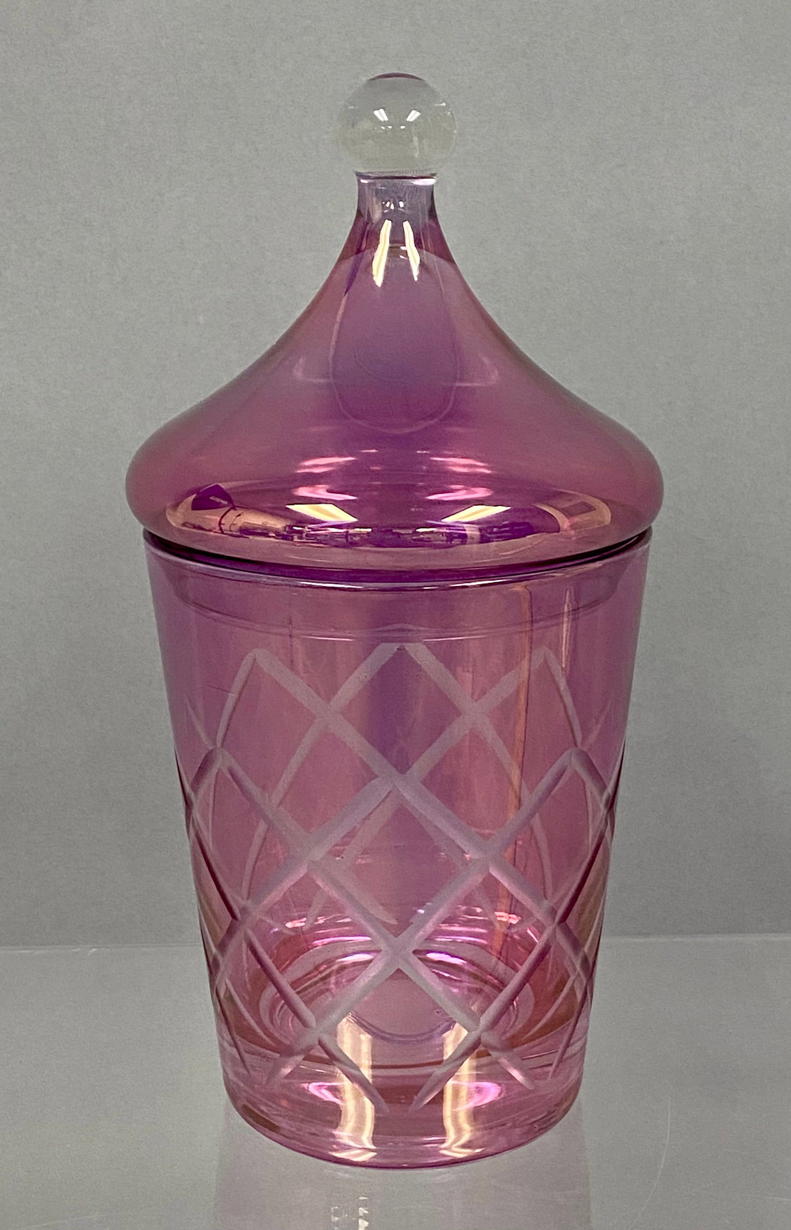 Amethyst Cut Glass Candy Jar: This amethyst-colored glass candy jar features a frosted hand-cut lattice pattern around the body. It is paired with a matching domed lid terminating in a clear spherical glass finial. No maker