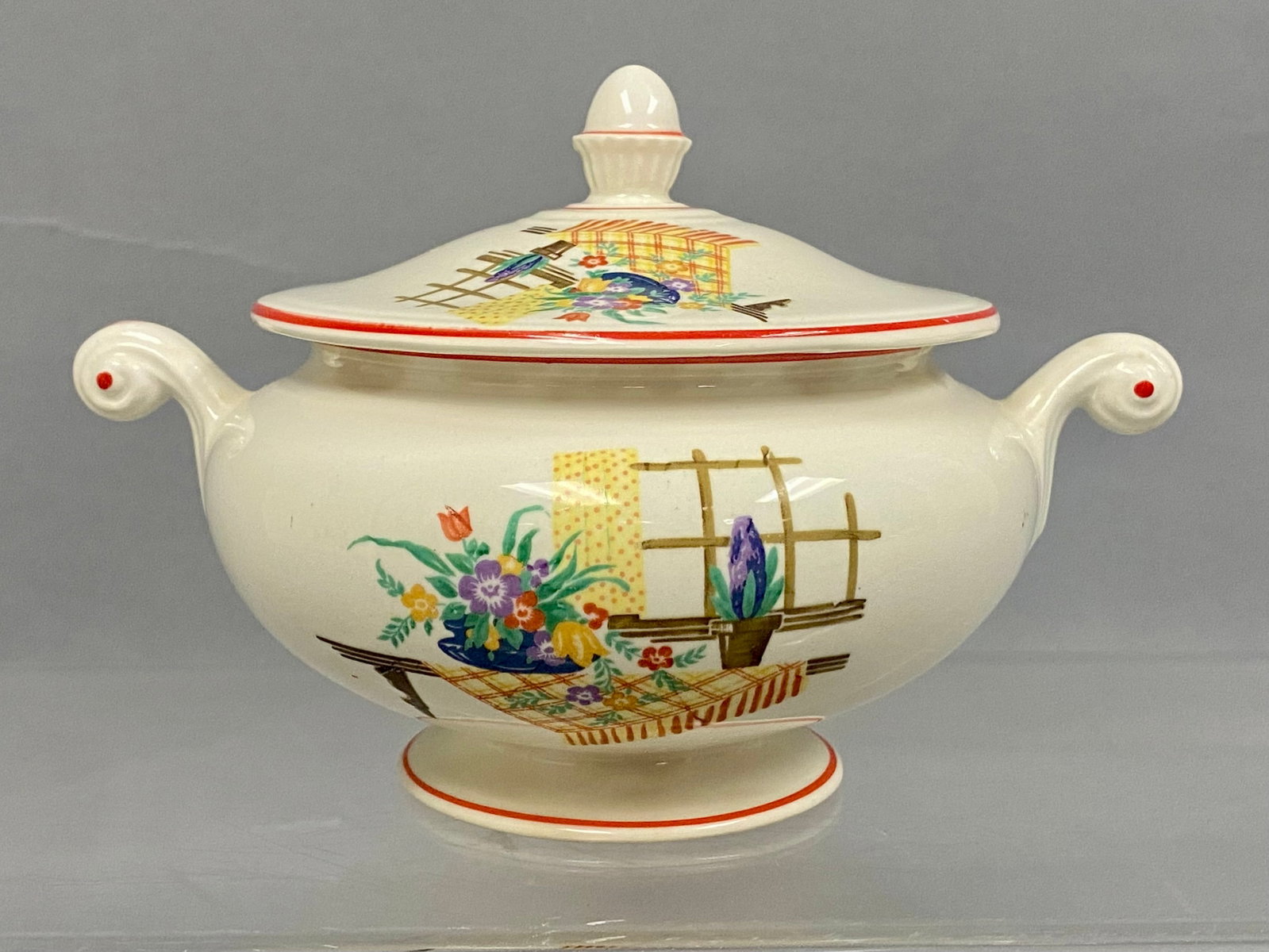 Homer Laughlin Eggshell Nautilus Sugar Bowl: This American semi-vitreous earthenware lidded sugar bowl features two scrolled handles and a footed base. The vessel is decorated with a transfer-printed kitchen scene of flowers on a plaid
