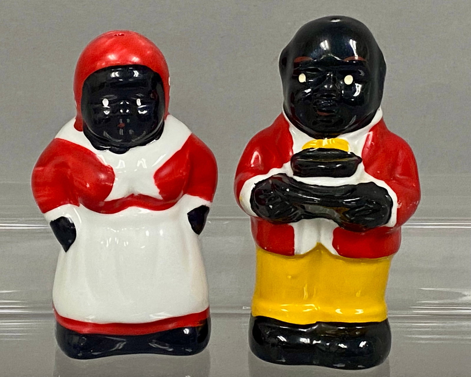 Japanese Ceramic Americana Salt & Pepper Shakers: A pair of vintage Japanese glazed ceramic salt and pepper shakers depicting stylized Americana figures. The female figure is modeled wearing a red headscarf and dress with a white collar and apron.