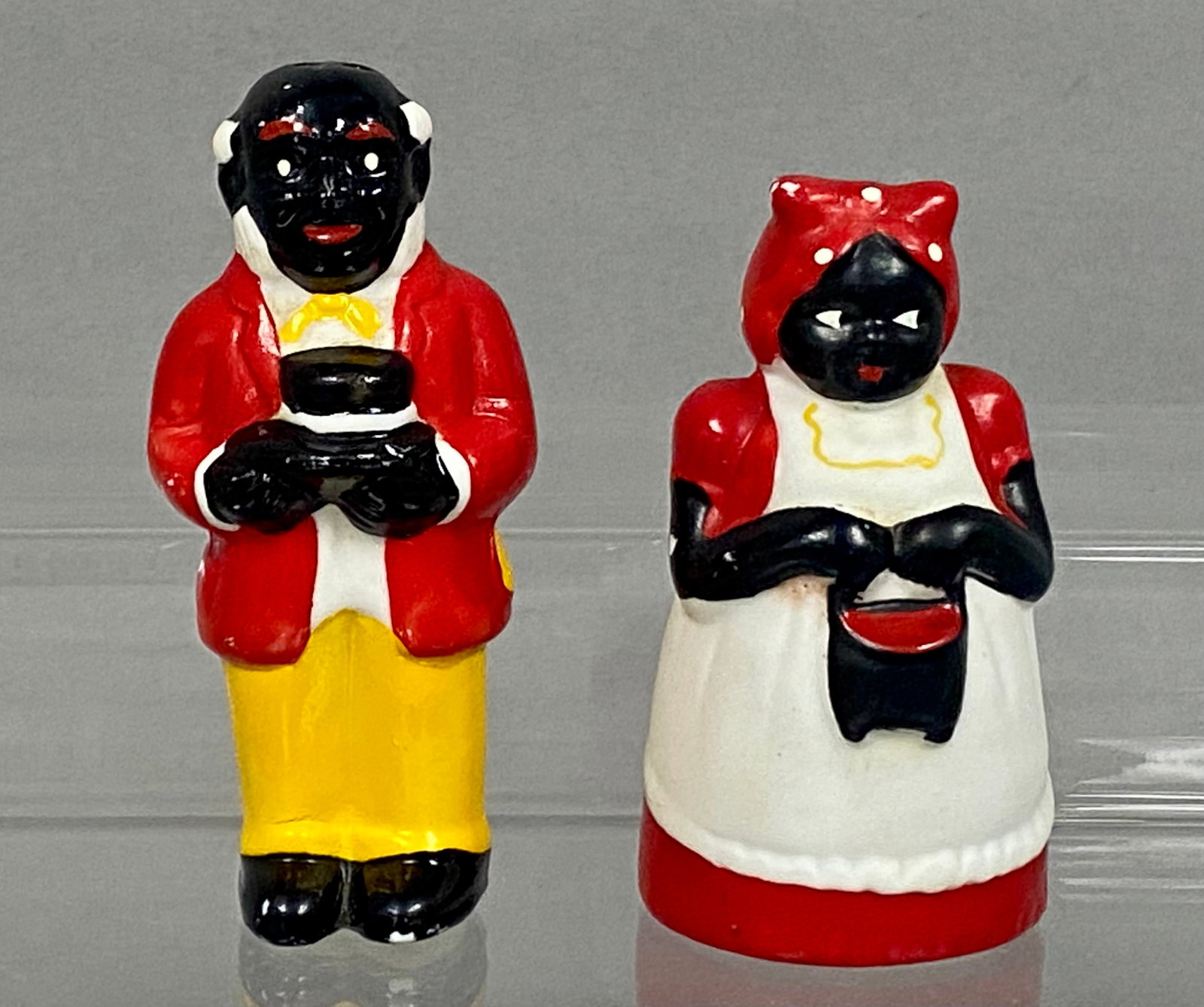Ceramic Black Americana Salt & Pepper Shakers: A pair of mid-century glazed ceramic salt and pepper shakers depicting stylized figures in the Black Americana tradition. The male figure is modeled in a red jacket, yellow trousers, and a white