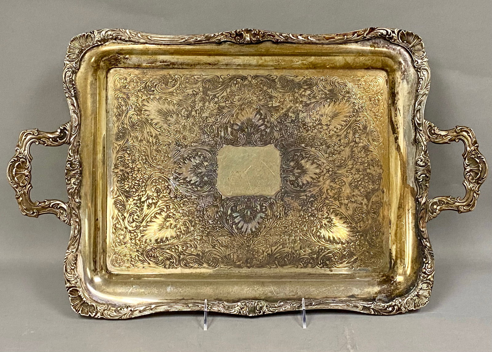 Wm Rogers Silver-Plated Rococo Handled Tray: This large rectangular serving tray is constructed of silver plate over a base metal, likely brass or copper. Executed in a Rococo Revival style, the piece features a wide, scalloped rim decorated