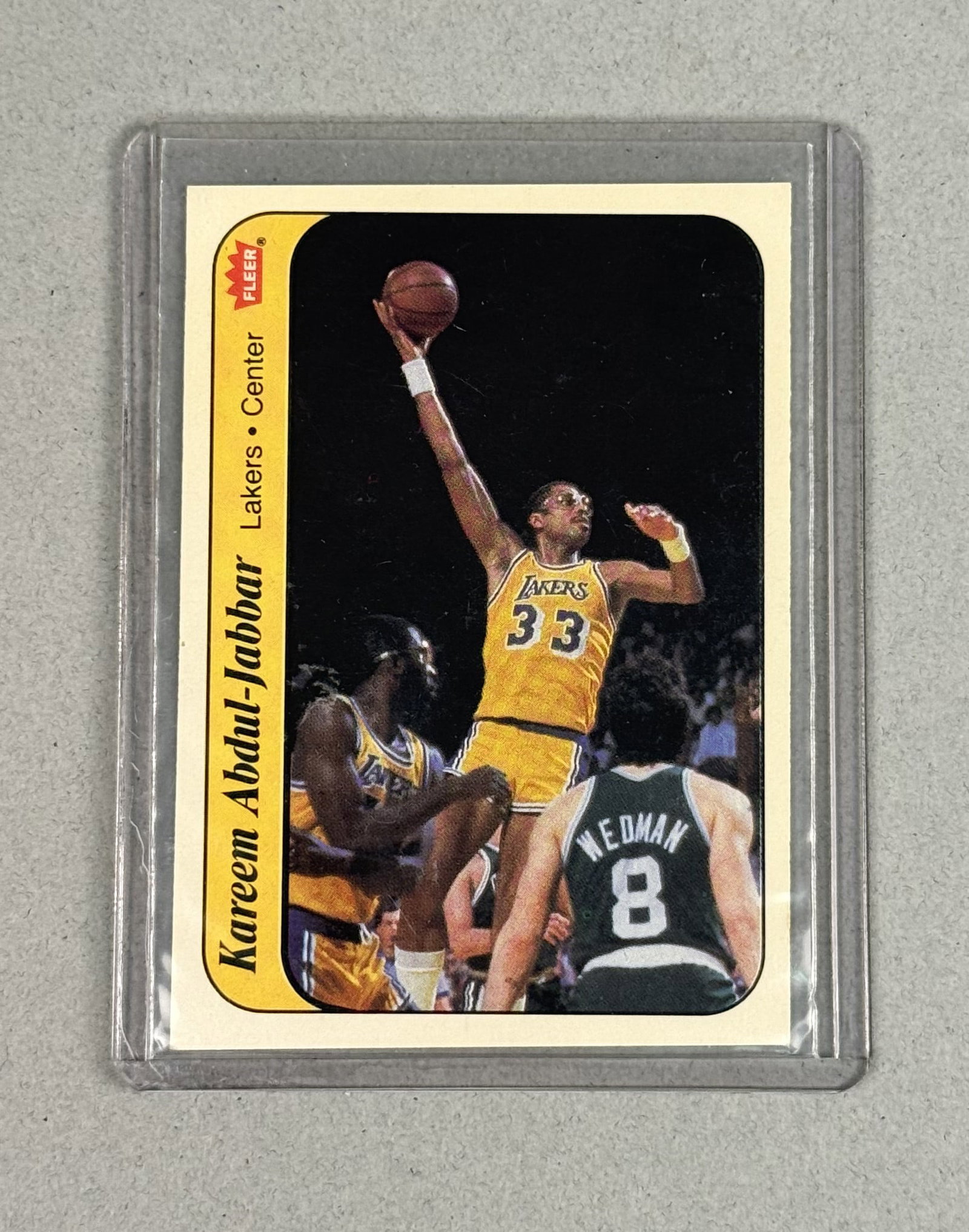1986 Fleer Kareem Abdul-Jabbar Unpeeled Sticker Card: An original 1986-87 Fleer basketball sticker insert featuring NBA Hall of Fame center Kareem Abdul-Jabbar. The front displays an action photograph of Abdul-Jabbar in his home Los Angeles Lakers jersey