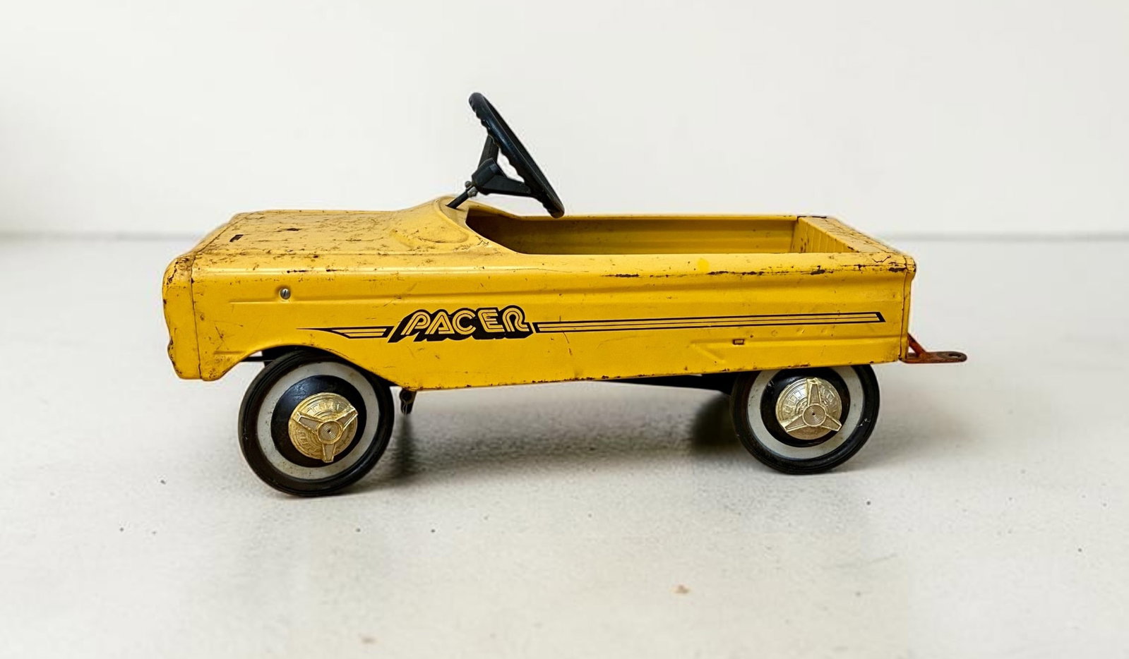 AMF Pacer Yellow Pedal Pickup Truck: A vintage pressed steel pedal car modeled as a pickup truck. The body is finished in yellow factory paint and features stylized black decals on both sides reading PACER underlined by three horizontal 