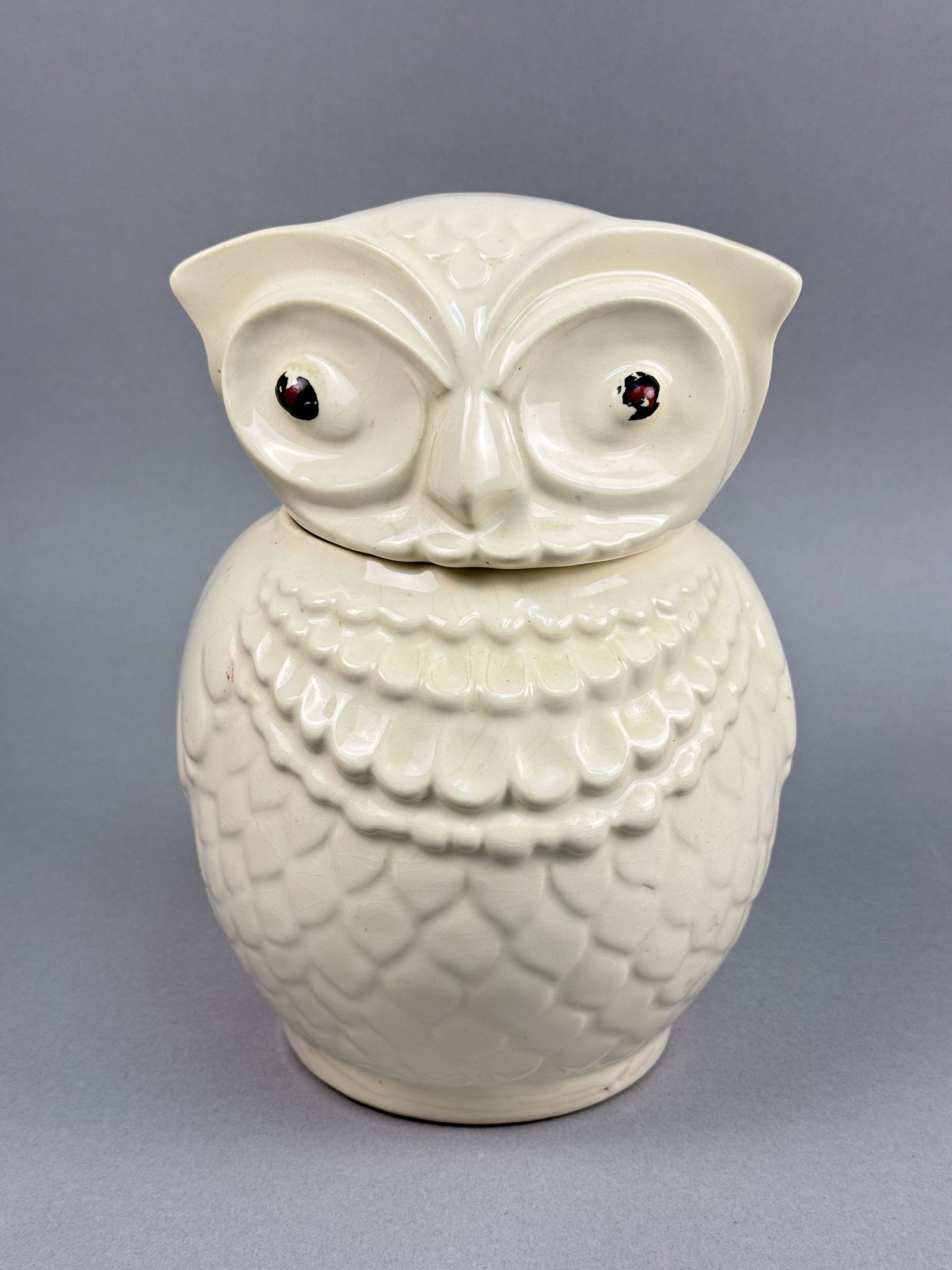 Glazed Ceramic Figural Owl Cookie Jar: This figural ceramic cookie jar is modeled in the form of a perched owl with a removable lid. The piece is constructed from earthenware finished in a glossy cream-colored glaze with molded relief