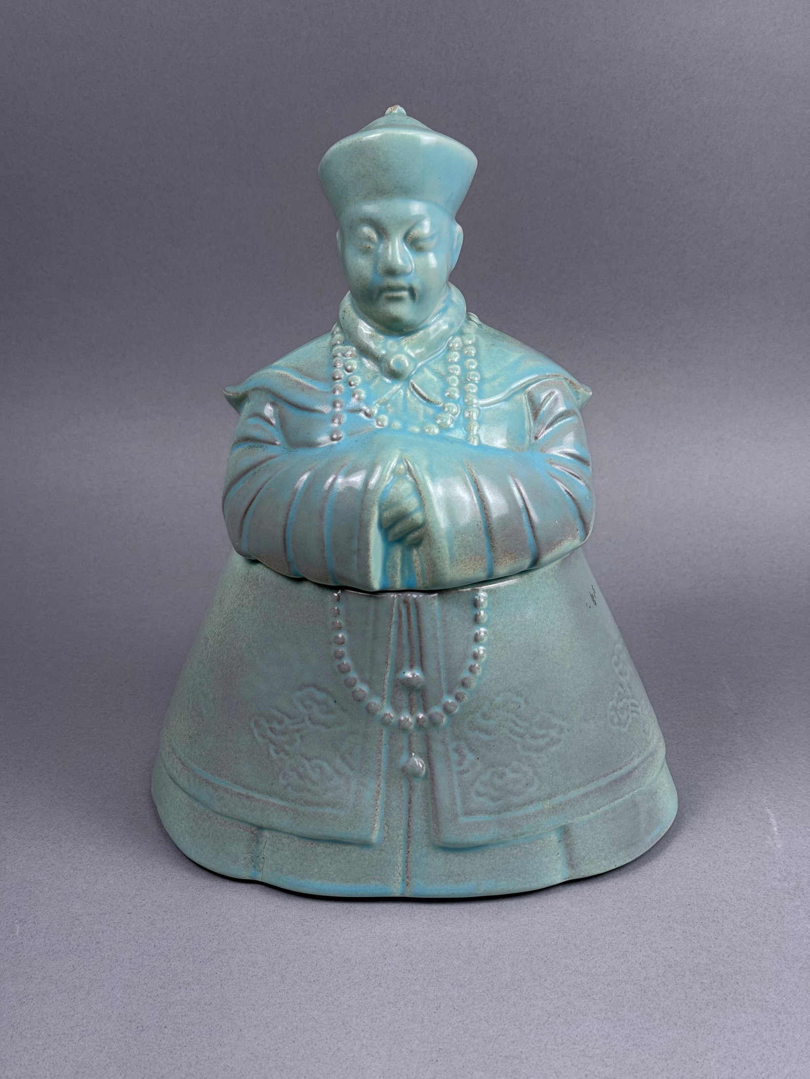 Turquoise Glazed Ceramic Emperor Cookie Jar: A two-piece ceramic container modeled in the form of a high-ranking Chinese official or imperial figure. The interior of both pieces is finished with a similar turquoise glaze. The piece is unmarked,