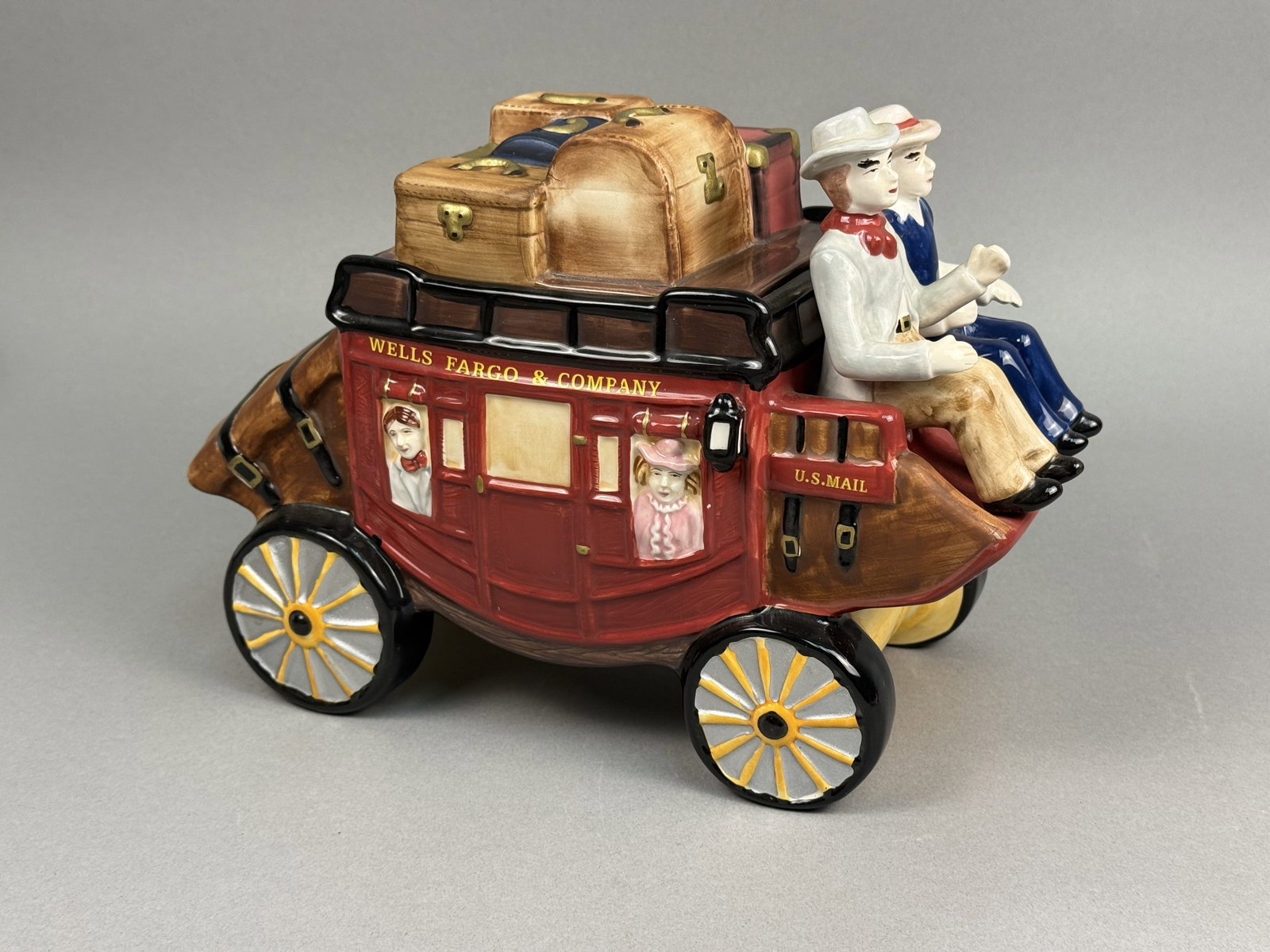 Wells Fargo Ceramic Stagecoach Cookie Jar: A lidded ceramic cookie jar modeled after a Wells Fargo & Company Overland Stagecoach. The glazed earthenware vessel is finished in a deep red palette with hand-painted yellow lettering reading WELLS