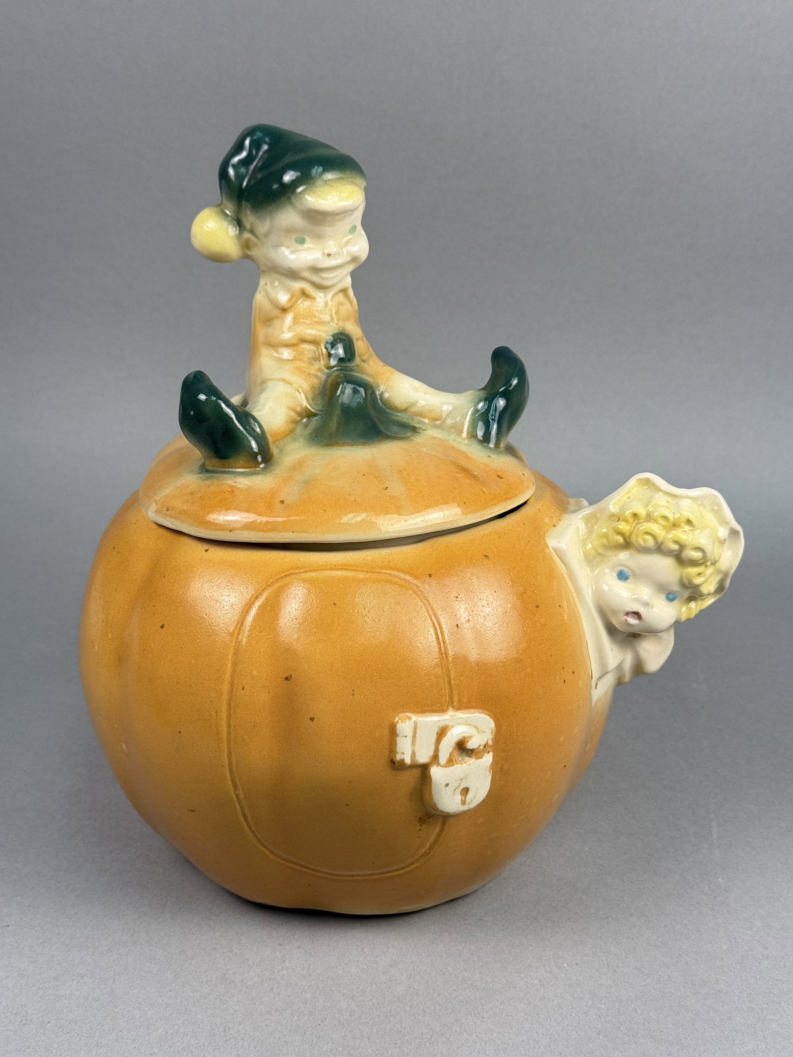 Ceramic Pumpkin Eater Cookie Jar: A figural American earthenware cookie jar designed in the form of a pumpkin house, inspired by the nursery rhyme Peter Peter Pumpkin Eater. The vessel features a mottled orange glaze with a molded