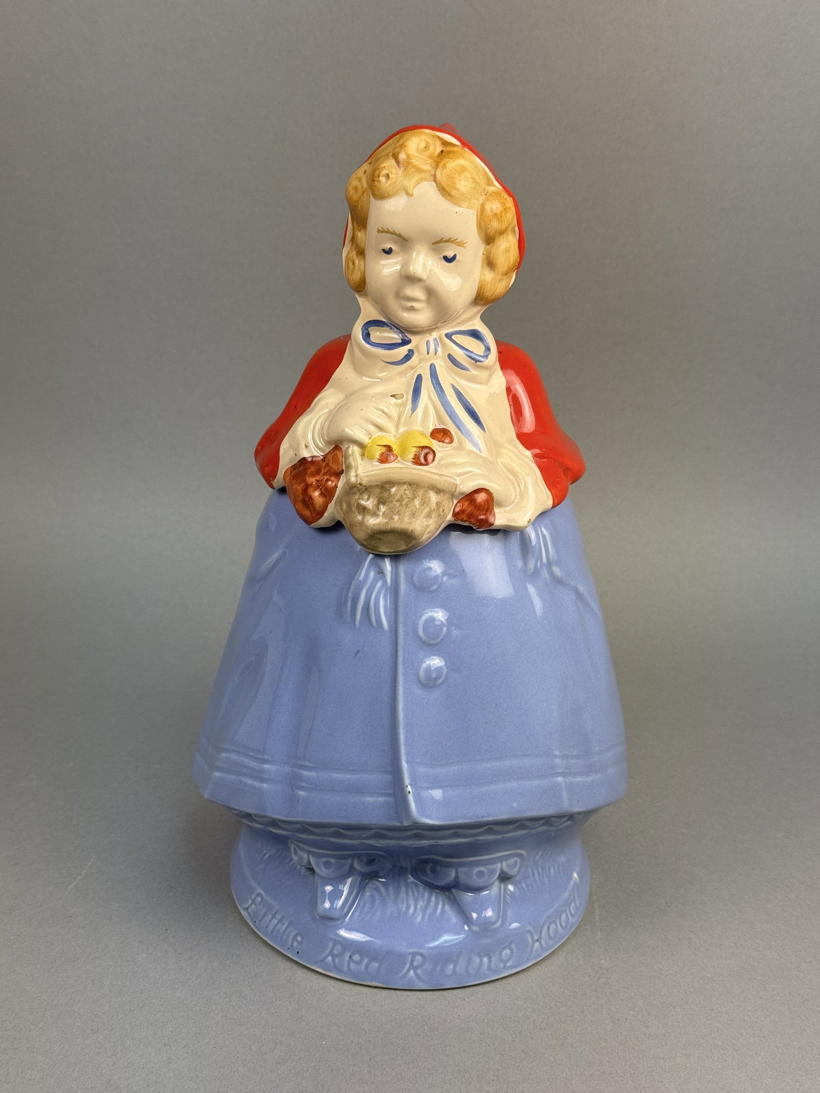 Little Red Riding Hood Ceramic Cookie Jar: A vintage two-piece figural earthenware cookie jar depicting the classic fairy tale character Little Red Riding Hood. The interior is finished in a coordinating blue glaze, and the unglazed underside
