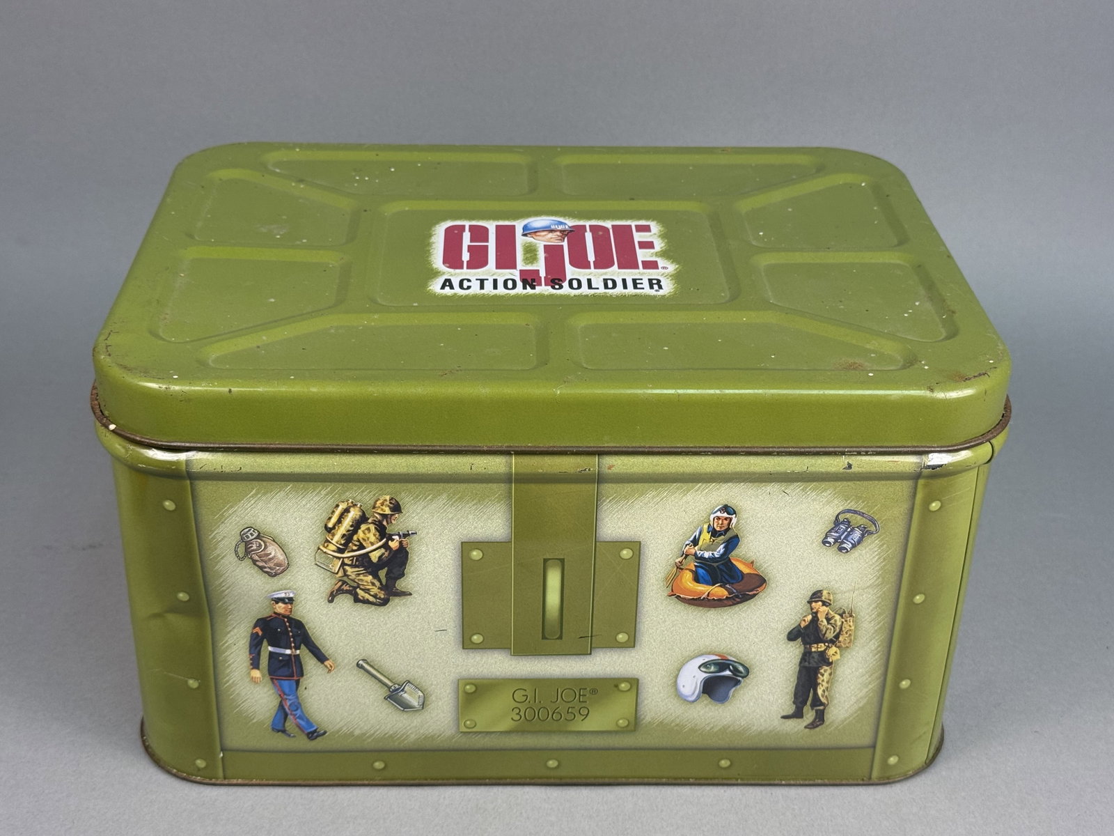 A.S.C. G.I. Joe Action Soldier Storage Tin: A collectible G.I. Joe Action Soldier themed tin storage box manufactured by A.S.C. in Lancaster, Pennsylvania, under license from Hasbro in 1998. The front panel bears a printed graphic of a metal pl