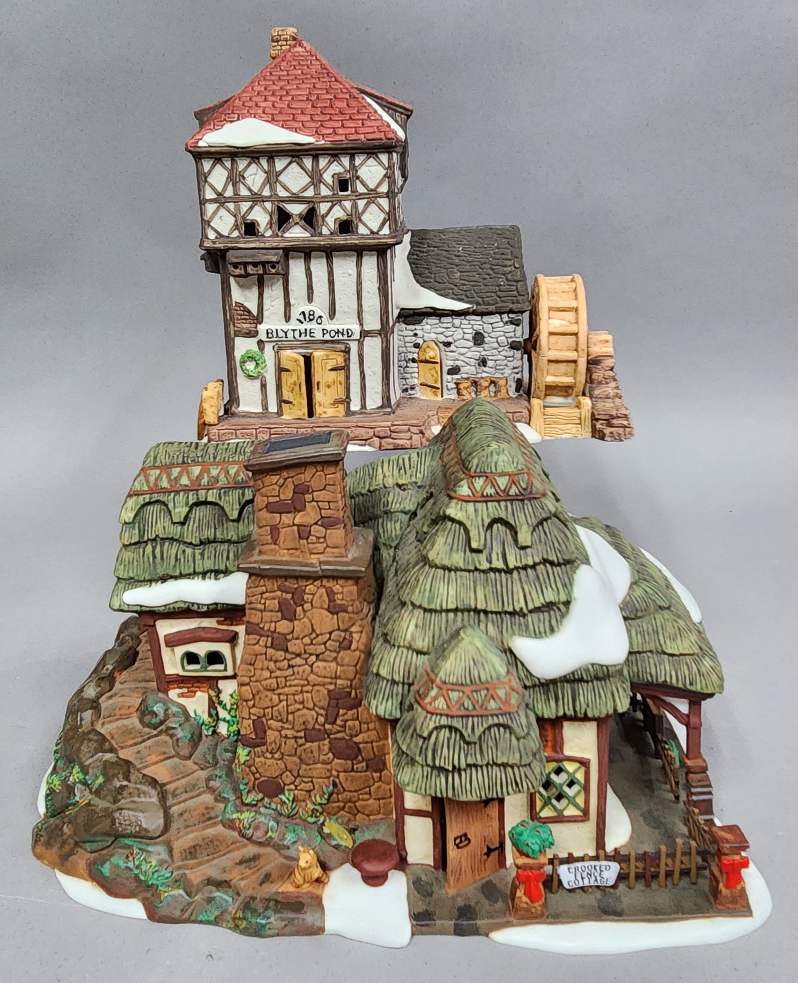 Department 56 Dickens Village Buildings: Two hand-painted porcelain buildings from the Department 56 Dickens' Village Series. The group includes the Crooked Fence Cottage, dated 1997, and the Blythe Pond mill, dated 1986. The base of the cot