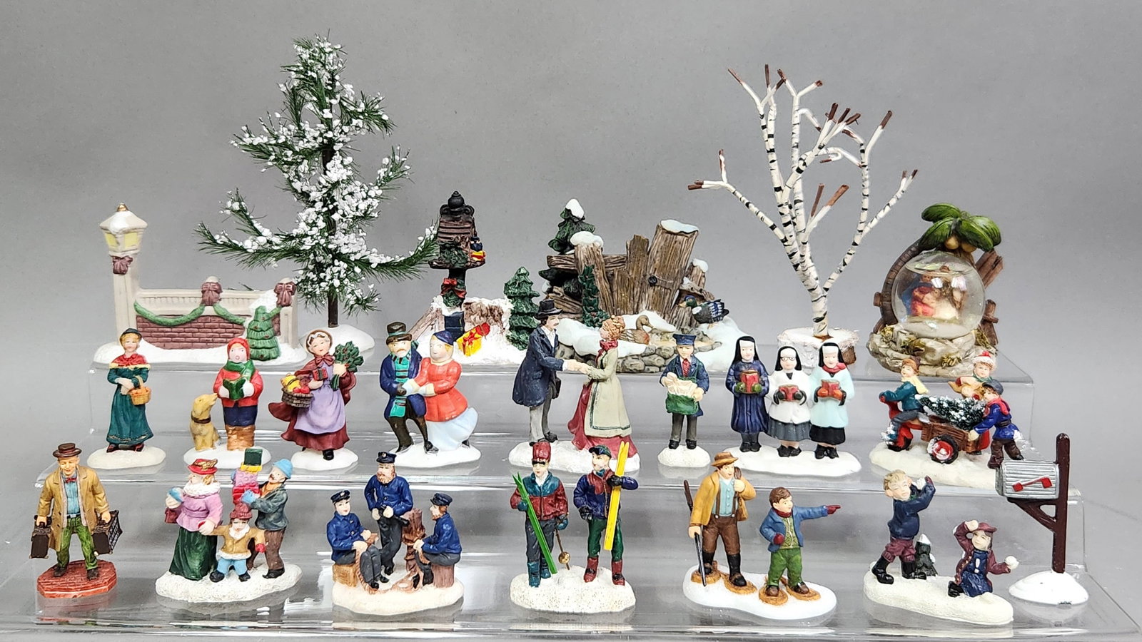 Winter Village Figurines & Scenery: An assortment of hand-painted resin and bisque porcelain figurines and landscape accessories designed for a holiday village display. The collection is in good overall condition, showing vibrant paint