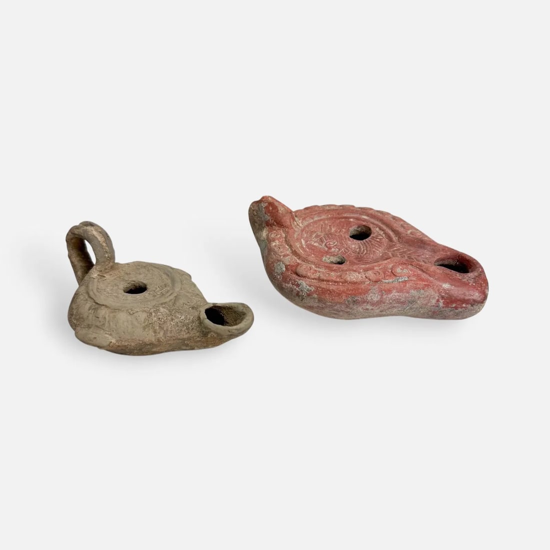 Two Ancient Roman Terra Cotta Redware Oil Lamps: Roman Empire, Imperial Period. Ca. 1st to 4th century CE. Repair near mouth to red oil lamp. Larger lamps measurements included in listing. Smaller lamp measures approx. 2" x 2 1/2" x 4".