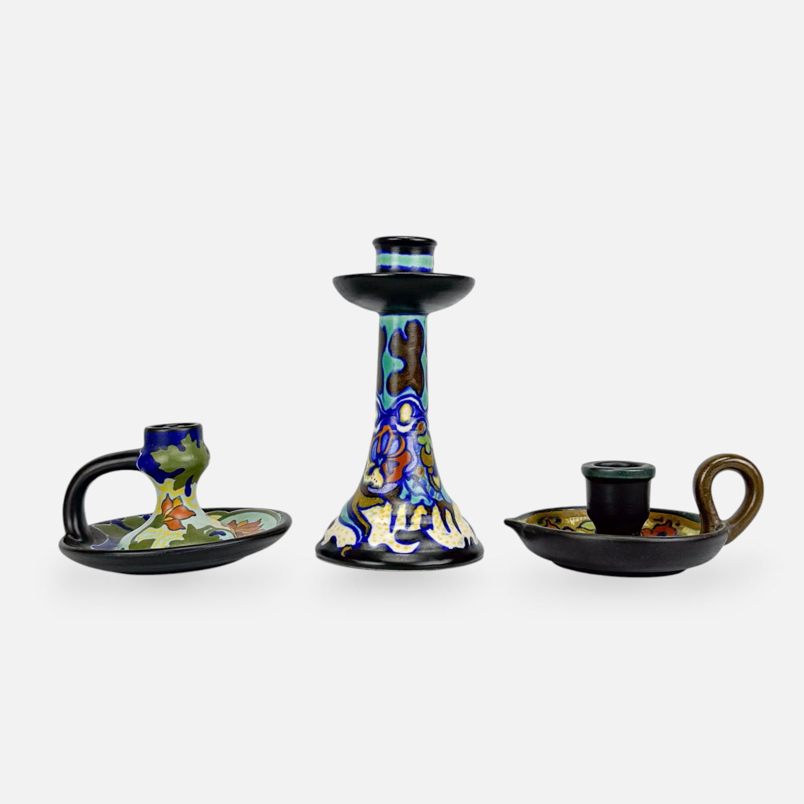 Three Gouda-Zuid Holland Art Pottery Candlesticks Chambersticks: Ca. early 20thC. Very good as shown, with minor age-appropriate surface wear. Free from any chips, cracks, or repairs. Tall candlestick dimensions included in listing. Smallest chambersticks measures