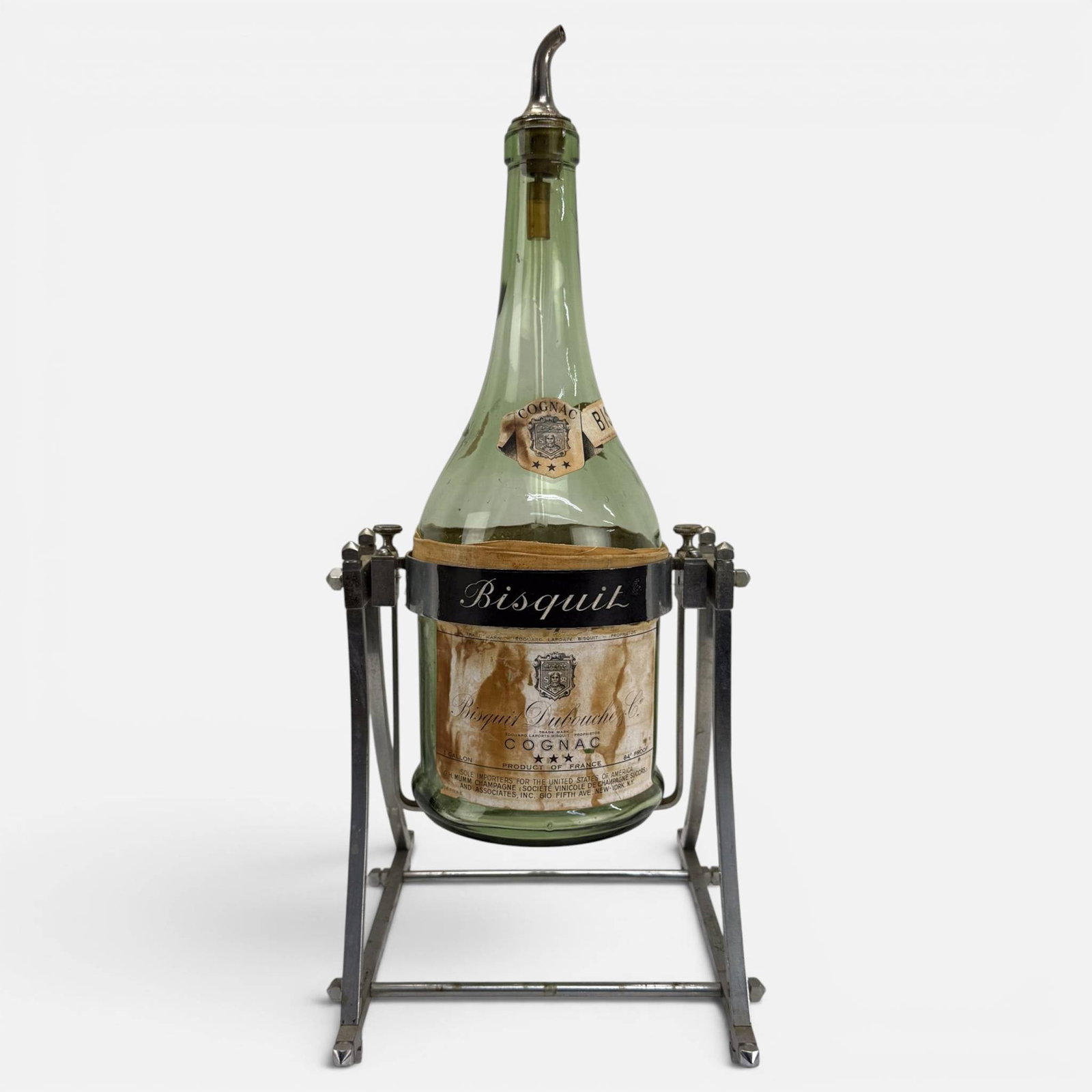 Bisquit Dubouche Cognac Promotional 1-Gallon Bottle Modernist Chrome Tilt Cradle: Ca. first half 20thC. Overall very good with dark stains on the paper label, no chips, cracks or repairs to glass or metal. Large display for a hotel or fancy restaurant, measuring approx. H: 24 1/2",