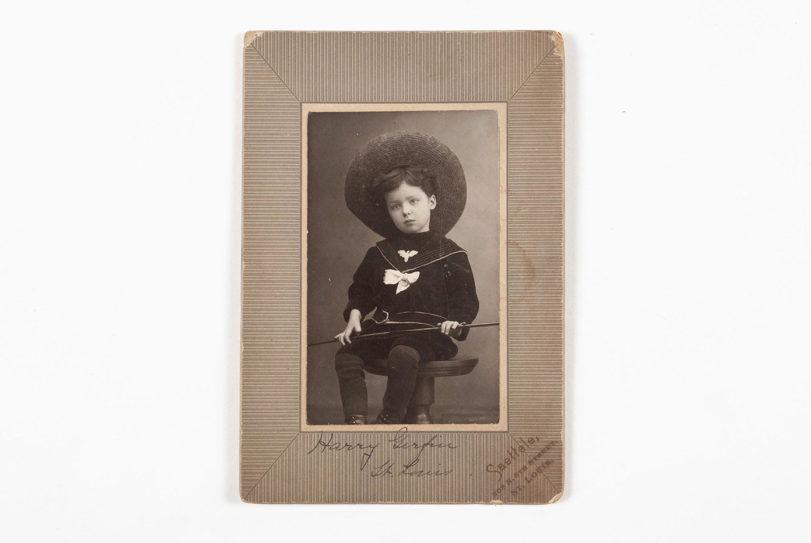 STUDIO PORTRAIT OF A ST. LOUIS CHILD: STUDIO PORTRAIT OF A ST. LOUIS CHILD American, early 20th century, gelatin. Portrait of a disenchanted young boy in sailor dress and hat, possibly a toy gun resting across his lap. "Harry Gerfin, St. 