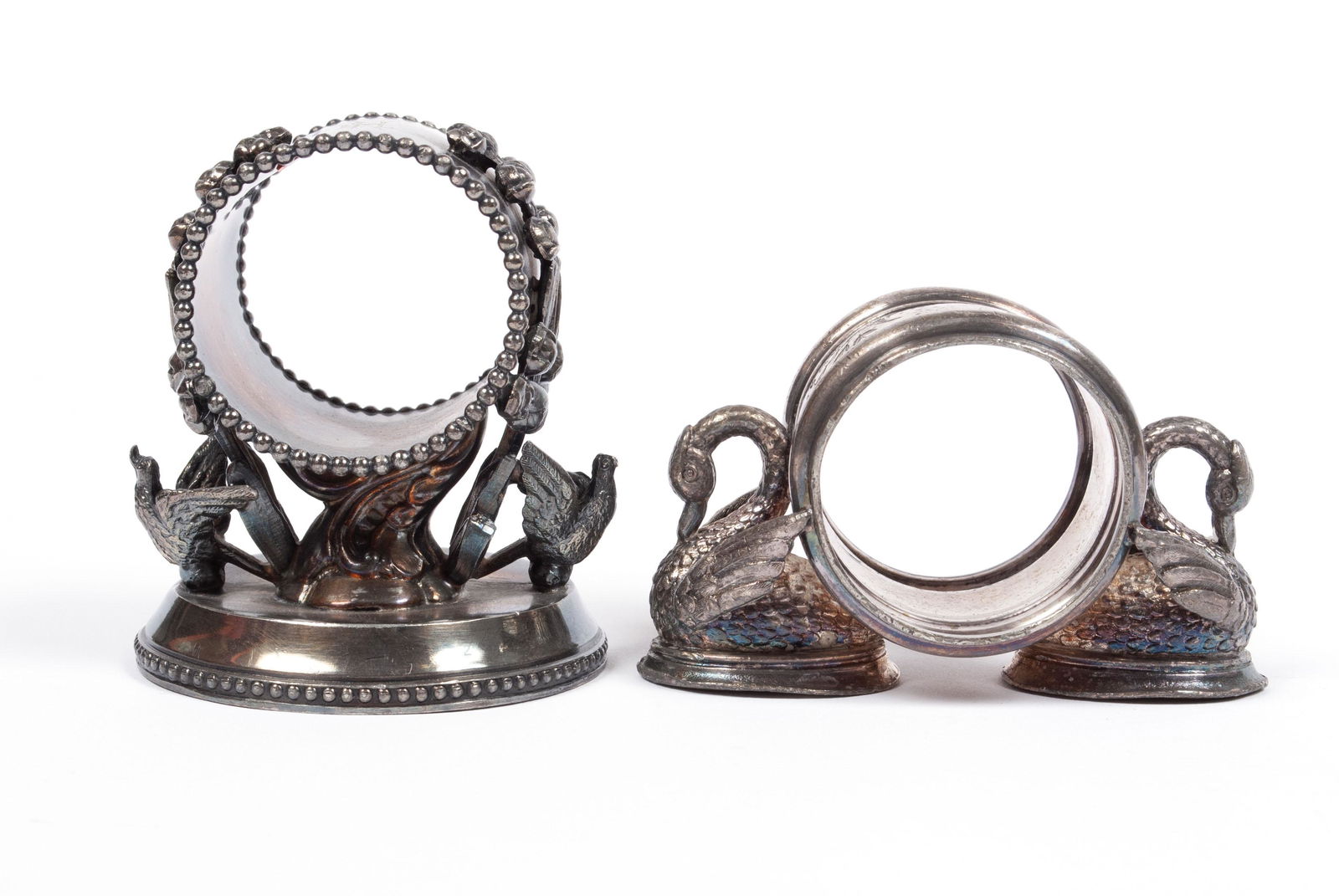 TWO BIRD-FLANKED NAPKIN RINGS: TWO BIRD-FLANKED NAPKIN RINGSRockford #83, two birds flanking a pedestaled ring decorated with budding flowers upon a circular base, 3" height, together with one unmarked ring with incised florals, fl