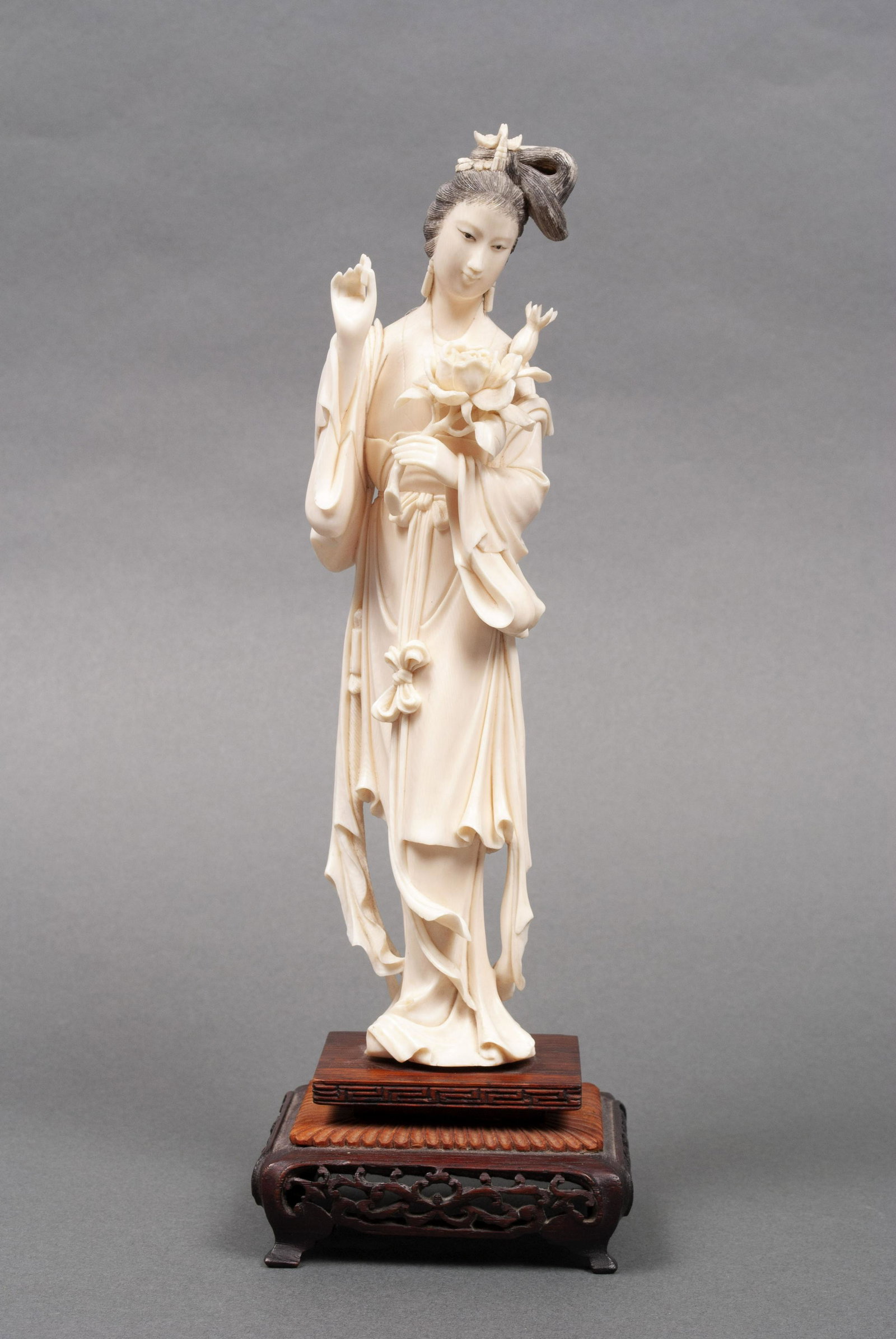 CARVING OF A BEAUTY: CARVING OF A BEAUTYEarly to mid-20th century, natural material. Female figure bearing a floral sprig, etched details to hair and pierced, footed wood base. 11.5" height