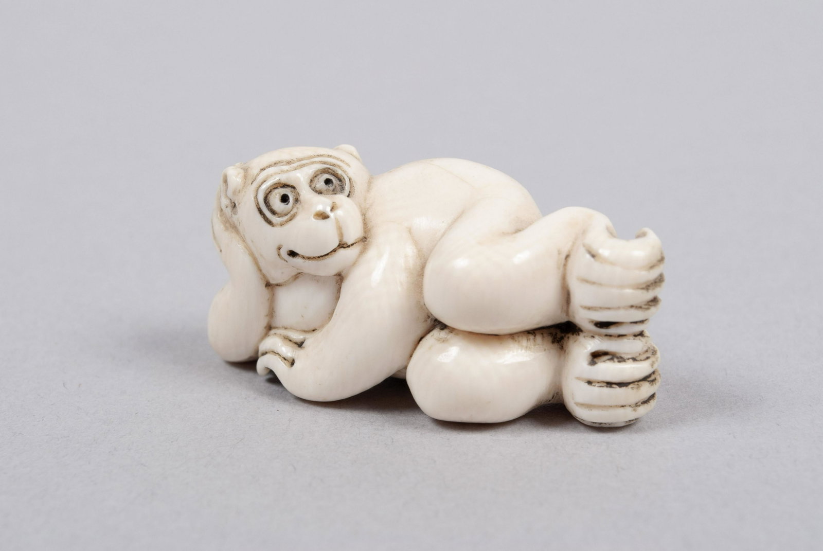 JAPANESE MONKEY NETSUKE: JAPANESE MONKEY NETSUKE Japan, early 20th century. A playful reclining monkey, signed to underside.