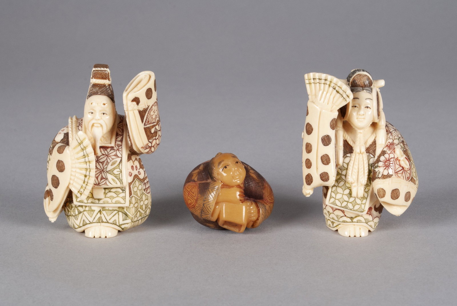 TRIO OF NETSUKE AND OKIMONO FIGURINES: TRIO OF NETSUKE AND OKIMONO FIGURINES Japan. A companion pair of man and woman okimono, finely detailed, polychrome incised patterns to their dress, both marked to underside, together with a composite