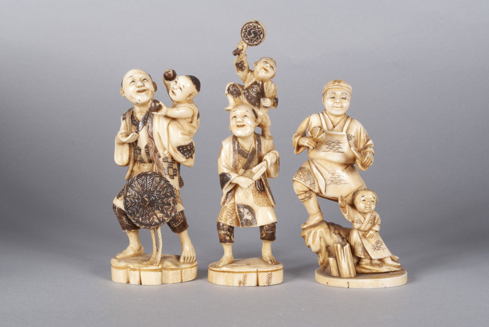 TRIO OF MAN AND CHILD OKIMONOS: TRIO OF MAN AND CHILD OKIMONOS Three finely carved standing figures, two of similar pose with the child riding on the man's back, mahogany coloration throughout the incised details. Together with anot