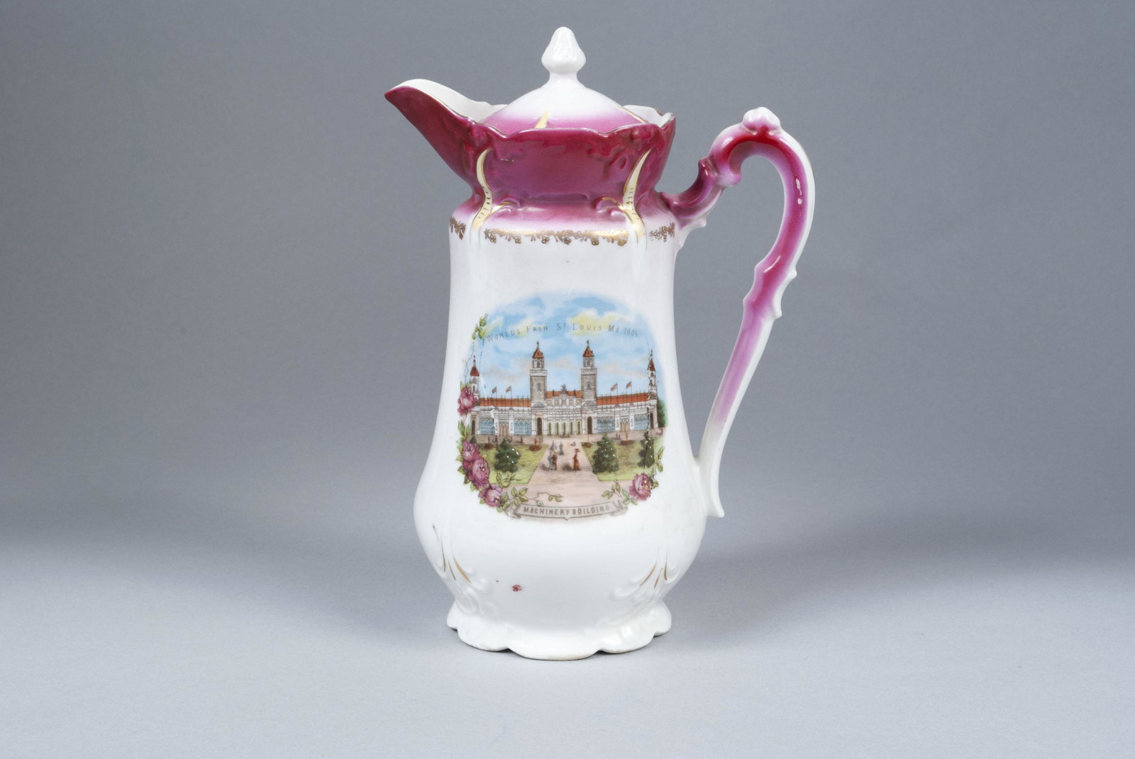 1904 ST. LOUIS WORLD'S FAIR PORCELAIN CHOCOLATE POT: 1904 ST. LOUIS WORLD'S FAIR PORCELAIN CHOCOLATE POTGerman, porcelain with pink neck, floral and gilt accents, transfer image of the Machinery Building to the body. 9.5" height