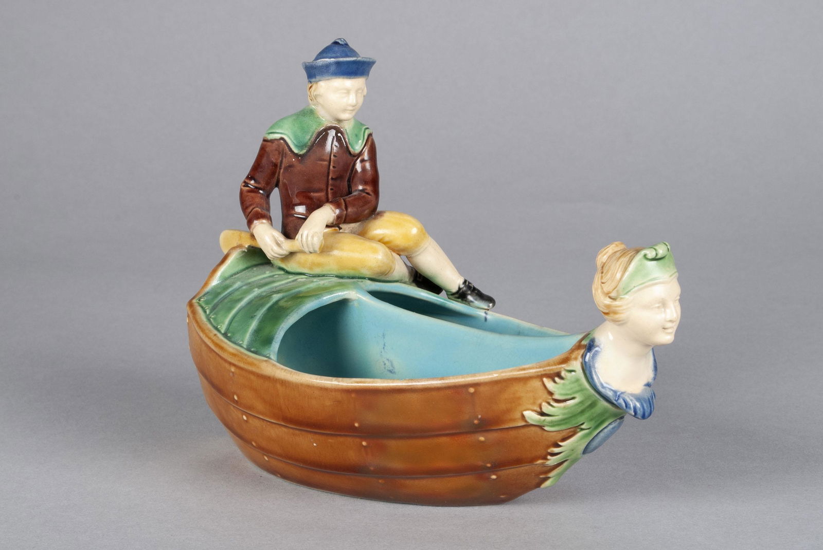 MAJOLICA MODEL OF A BOY AND BOAT BY MINTON: MAJOLICA MODEL OF A BOY AND BOAT BY MINTONEngland, 1865, divided dish modelled as a boat with boy at helm having female bust prow, impressed marks underfoot, pattern number 507. 4.75" height, 6.75" wi