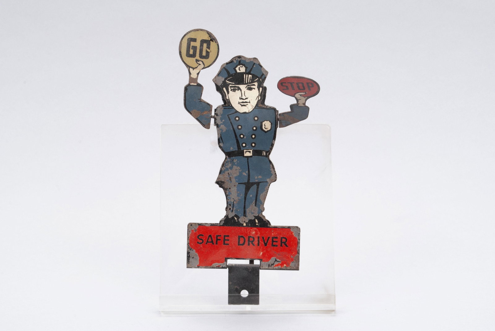 "SAFE DRIVER" POLICEMAN FIGURAL LICENSE PLATE TOPPER: "SAFE DRIVER" POLICEMAN FIGURAL LICENSE PLATE TOPPER Metal, early 20th century. Full figure of a police officer with articulated arms showing "GO" when you step on the gas, and "STOP" when you step on