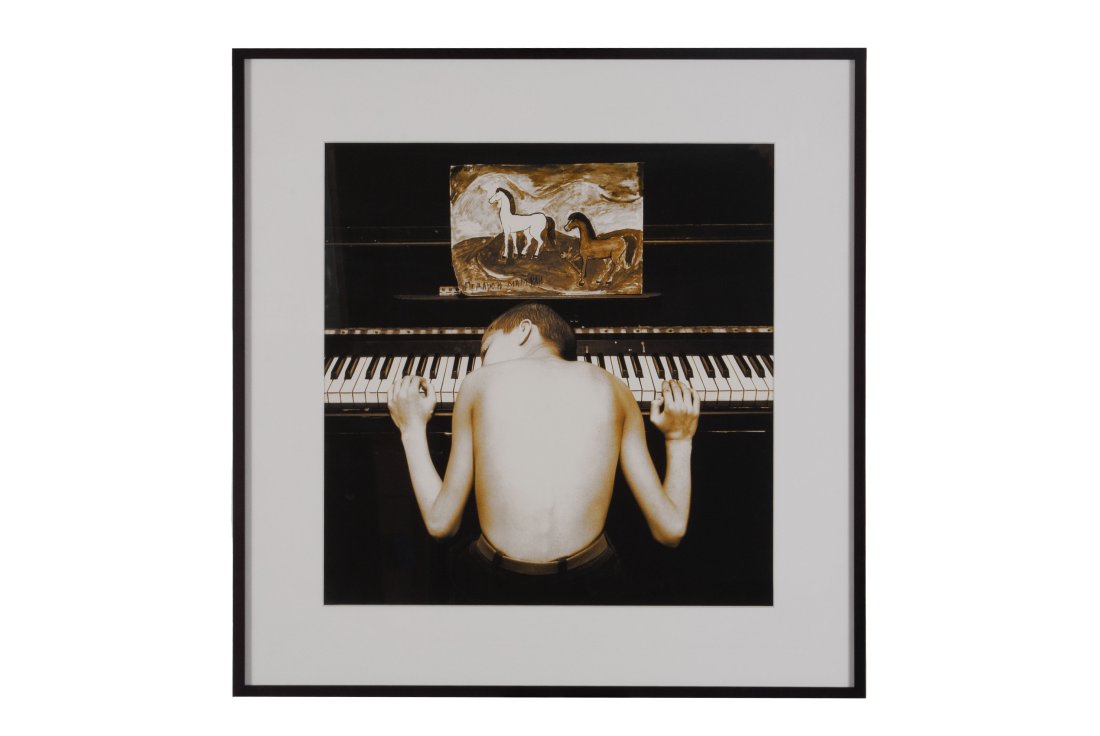 EVGENY MOKHOREV (RUSSIAN, B. 1967): Untitled (Pause), c. 1992.Silver gelatin print, notations to verso. A young boy hunched over a piano, the standee bearing a small painting of two horses. Matted behind glass, ebonized frame.Sight: 15.