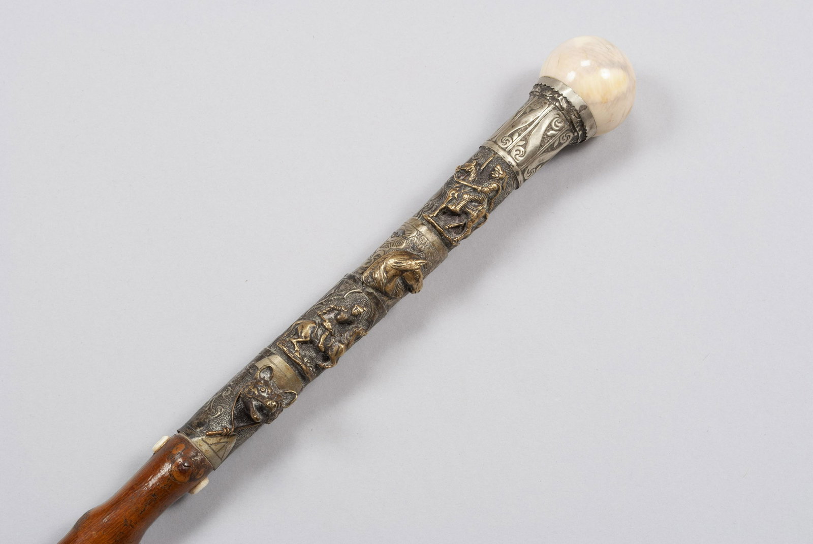A HUNTING THEMED WALKING STICK/CANE: A HUNTING THEMED WALKING STICK/CANE With polished ball finial, wrapped in hammered silver with extruding Shakespearean knightly and equestrian brass figures along with fox head, upon a lacquered, natu