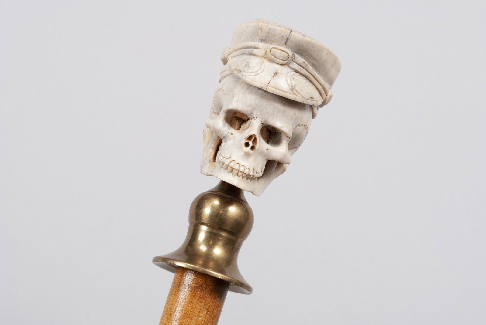 CARVED MEMENTO MORI WALKING STICK/CANE: CARVED MEMENTO MORI WALKING STICK/CANE Likely mid-century. The large finial in the form of a full skull in hat, the top with natural texture, and mounted to brass collar on a lacquered bamboo shaft. 3
