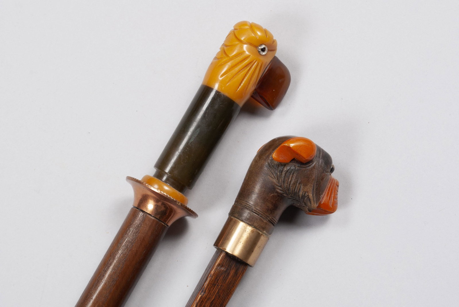 PAIRING OF BAKELITE AND WOODEN WALKING STICKS/CANES: PAIRING OF BAKELITE AND WOODEN WALKING STICKS/CANES The finials in the forms of a parrot and a bulldog, the bulldog with a wooden head, amber muzzle and ears. Both with glass eyes, the parrot with cop