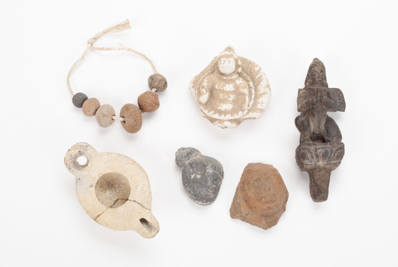 SIX (6) ANTIQUITIES: SIX (6) ANTIQUITIES Consisting of a Mathura fragmentary red stone head, a Crete oil lamp (repaired), three (3) deity/Buddha figures and a strand of six clay beads. 1.25" to 5.5" heights