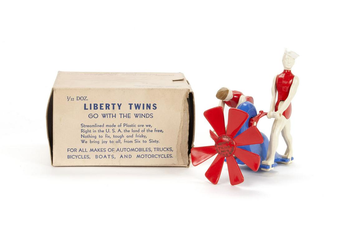LIBERTY TWINS RED WHITE AND BLUE HOOD ORNAMENT MASCOT WITH ORIGINAL BOX: LIBERTY TWINS RED WHITE AND BLUE HOOD ORNAMENT MASCOT WITH ORIGINAL BOX American, ca. 1940 , plastic, by Action Novelty Inc. Interactive ornament showing two figures in military caps cranking as natur