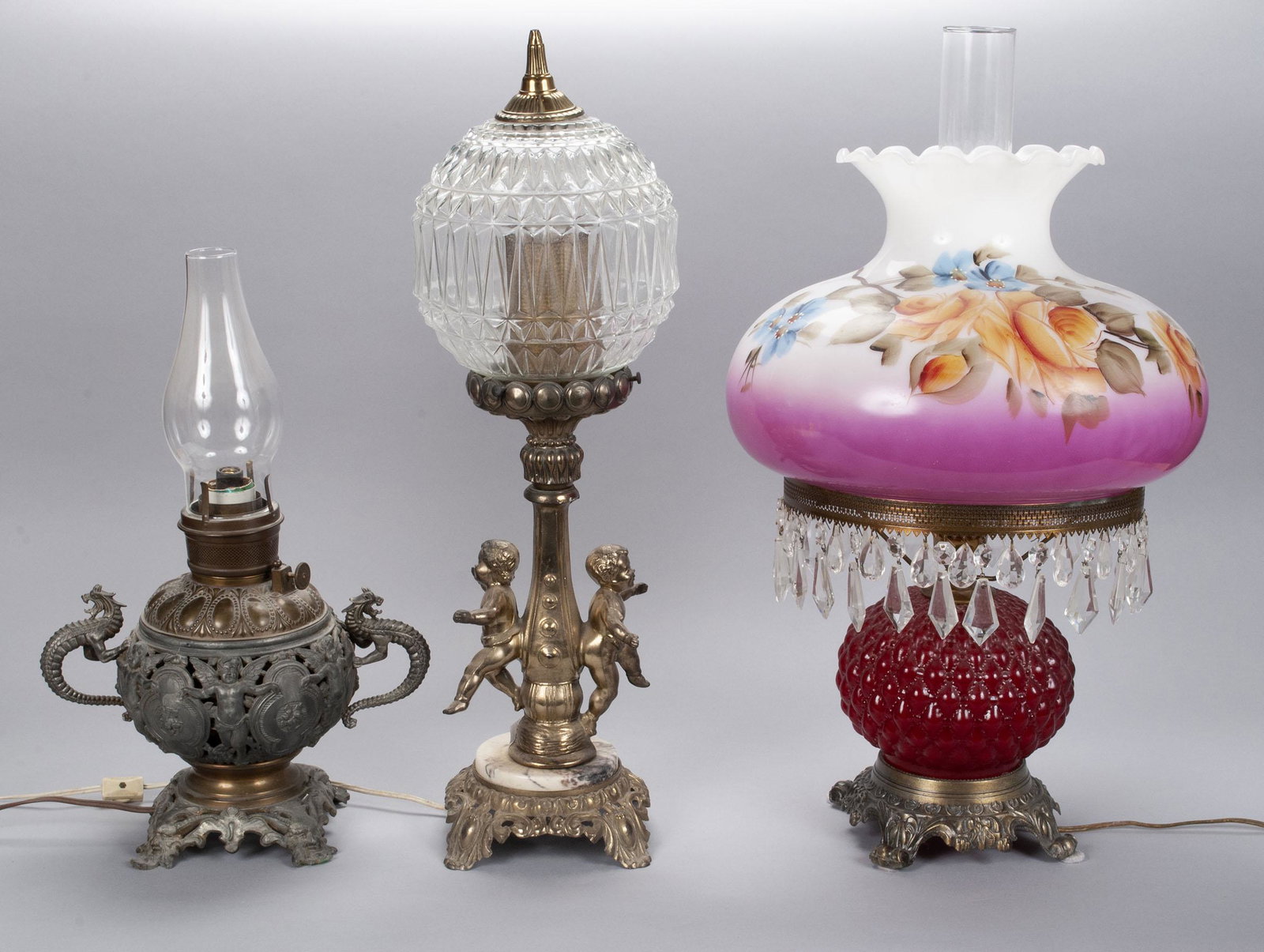 TRIO OF ORNATE LAMPS: TRIO OF ORNATE LAMPS Three (3) lamps from the early to mid-20th century; including one American Victorian double dragon kerosene lamp, New York manufactured; one double putti globe glass shade lamp on