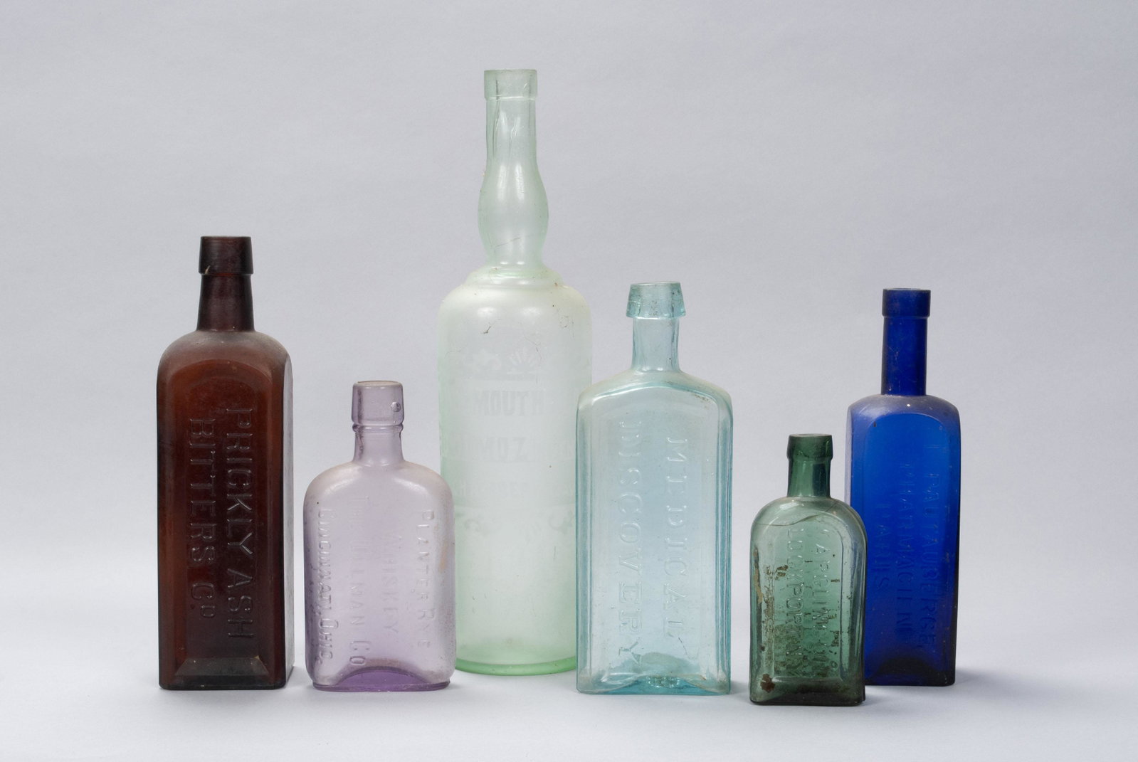 SIX ANTIQUE TINTED GLASS BOTTLES: SIX ANTIQUE TINTED GLASS BOTTLES Mostly American, early 20th century. Including Prickly Ash Bitters Co.; Gargling Oil: Lockport, NY; L. Pautauberge Pharmasien, Paris; Planter Rye Whiskey: The Ullman C