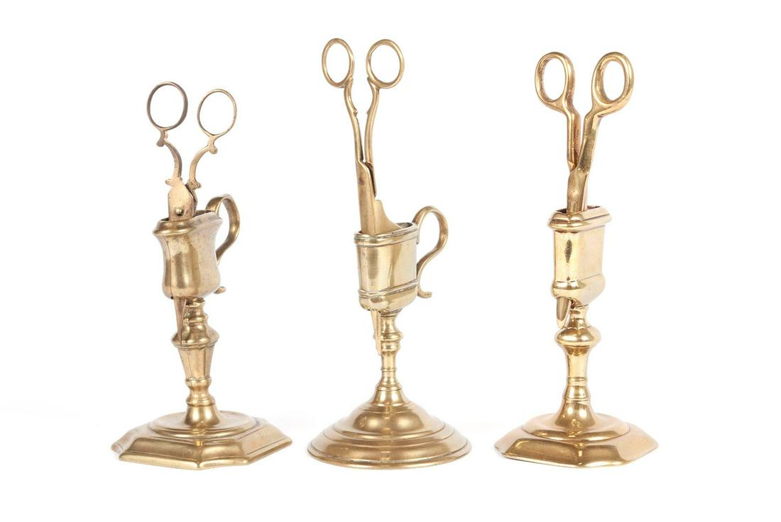 THREE ENGLISH BRASS CANDLE WICK SNIPPERS ON STANDS: THREE ENGLISH BRASS CANDLE WICK SNIPPERS ON STANDS19th century. Formal snippers on fitted stands.Tallest: 8 1/2 in. (21.59 cm.)