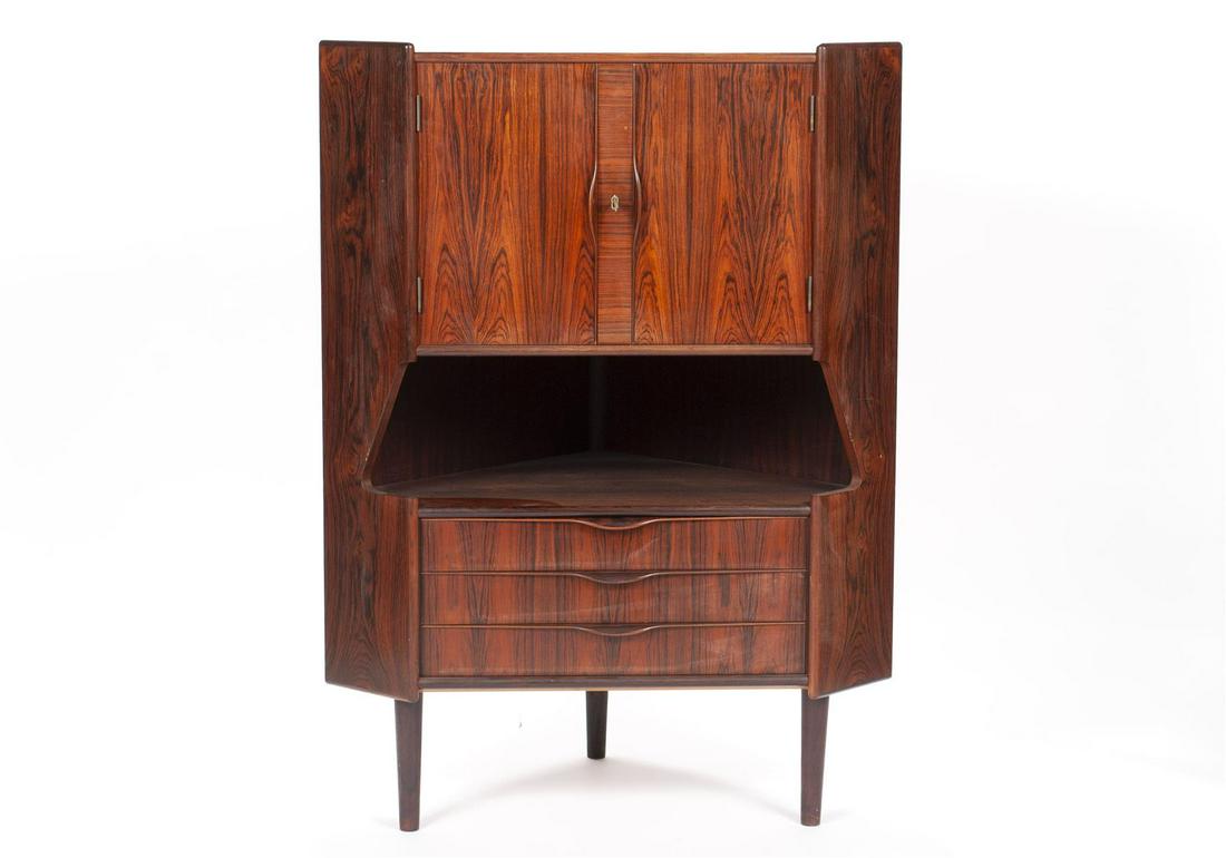 OMANN JUN ROSEWOOD CORNER CABINET: OMANN JUN ROSEWOOD CORNER CABINETDenmark, mid-20th century. Cupboard doors cover the pattern mirrored interior, over the open shelf with three drawers below, and terminating on tapering cylindrical le
