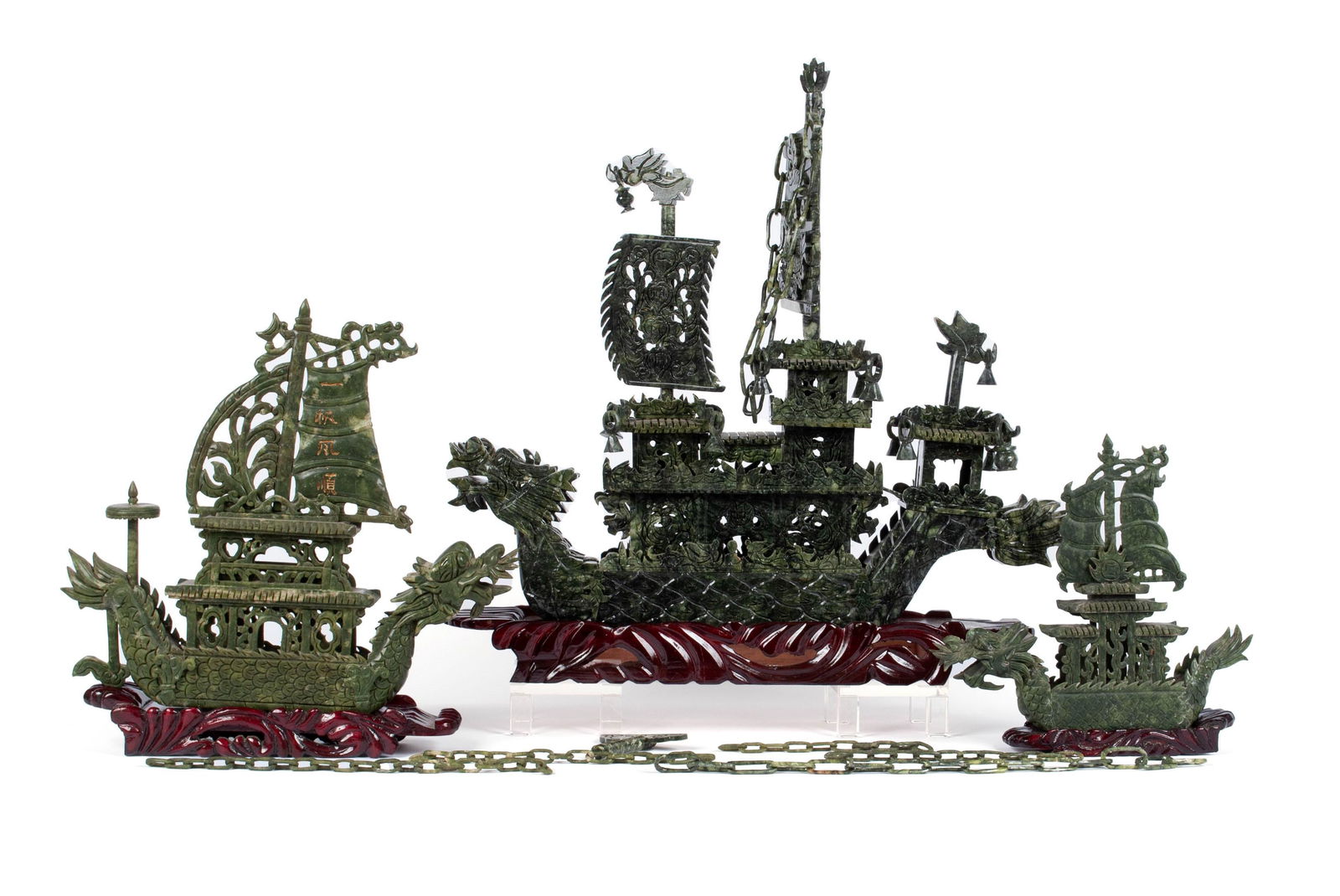THREE-PIECE FLOTILLA OF SPINACH JADE: THREE-PIECE FLOTILLA OF SPINACH JADEChinese, 20th century, jade. Three ships with dragon form prows, elaborately figured and reticulated sails and construction, atop wave form bases and accompanied by