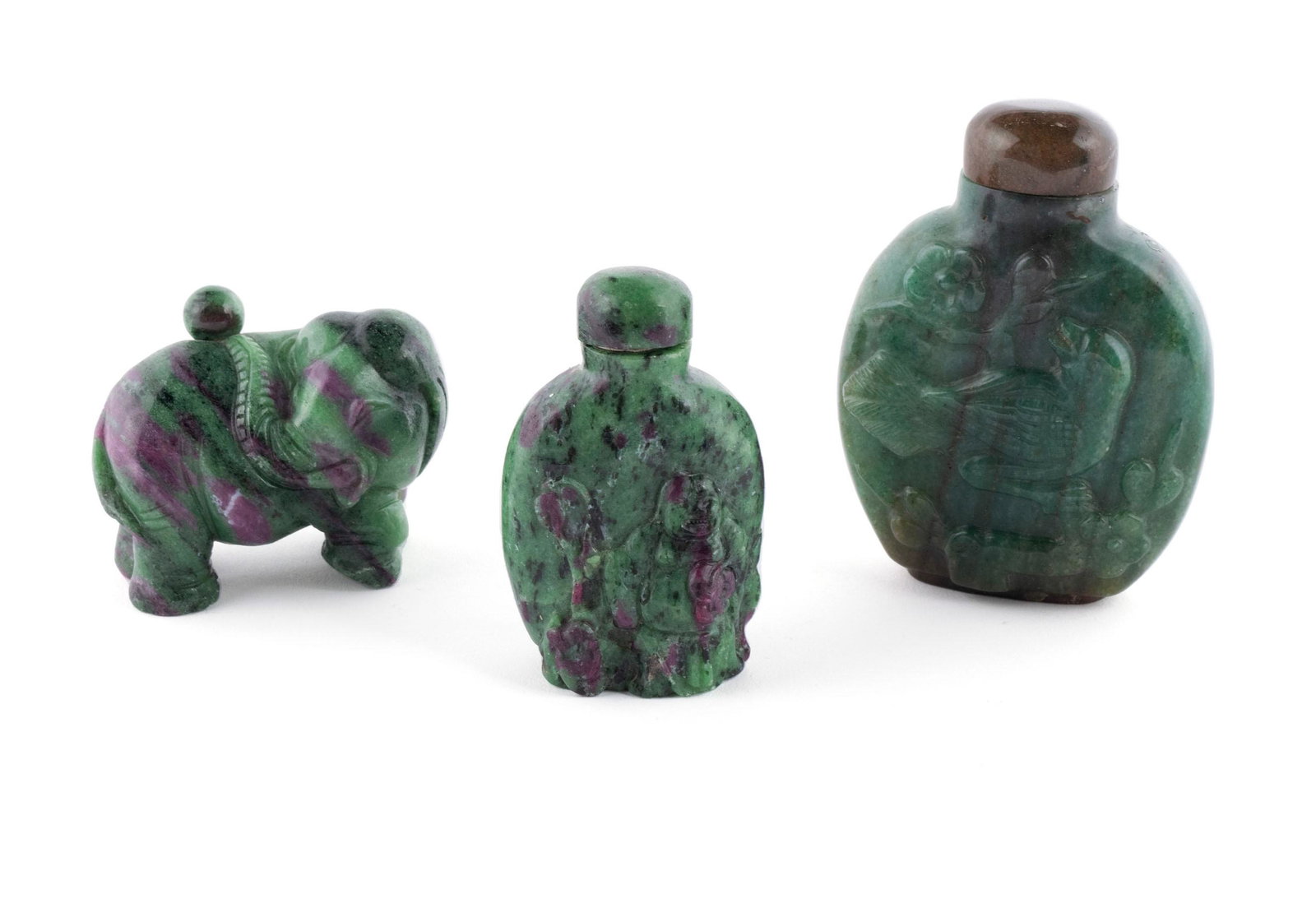 THREE FUCHSITE & RUBY ZOISITE CARVED SNUFF BOTTLES: THREE FUCHSITE & RUBY ZOISITE CARVED SNUFF BOTTLES Chinese, mid-20th century. The first of ruby zoisite in rich green color with ruby mottling, carved in relief as a Hotei with coins, the stopper matc