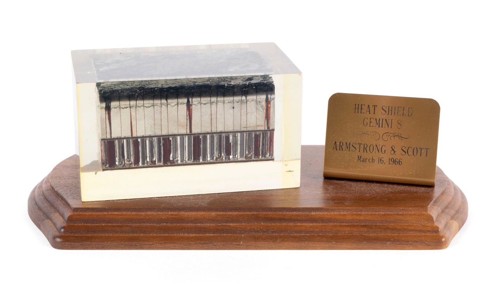 A GEMINI VIII (NEIL ARMSTRONG & DAVID SCOTT) HEAT SHIELD IN PLEXIGLASS: A GEMINI VIII HEAT SHIELD IN PLEXIGLASSMounted to a wooden base aside metal plaque reading "Heat Shield, Gemini 8; Armstrong & Scott, March 16th, 1966".3 1/2 x 5 x 10 in. (8.9 x 12.7 x 25.4 cm.)