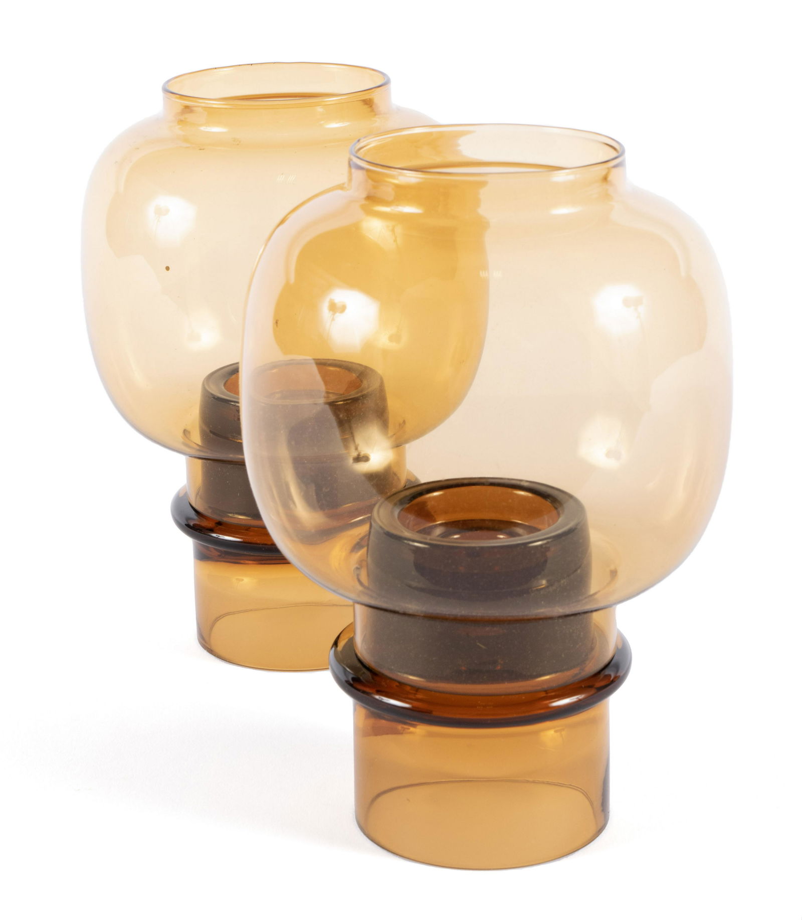 CANDLEHOLDERS BY HEIKKI ORVOLA FOR WARTSILA ARABIA: CANDLEHOLDERS BY HEIKKI ORVOLA FOR WARTSILA ARABIAFinnish, 1974 design, glass. A pair of hurricane shade Tuikku candleholders in amber, stickers still intact.7 1/2 x 5 in. (19.1 x 12.7 cm.)