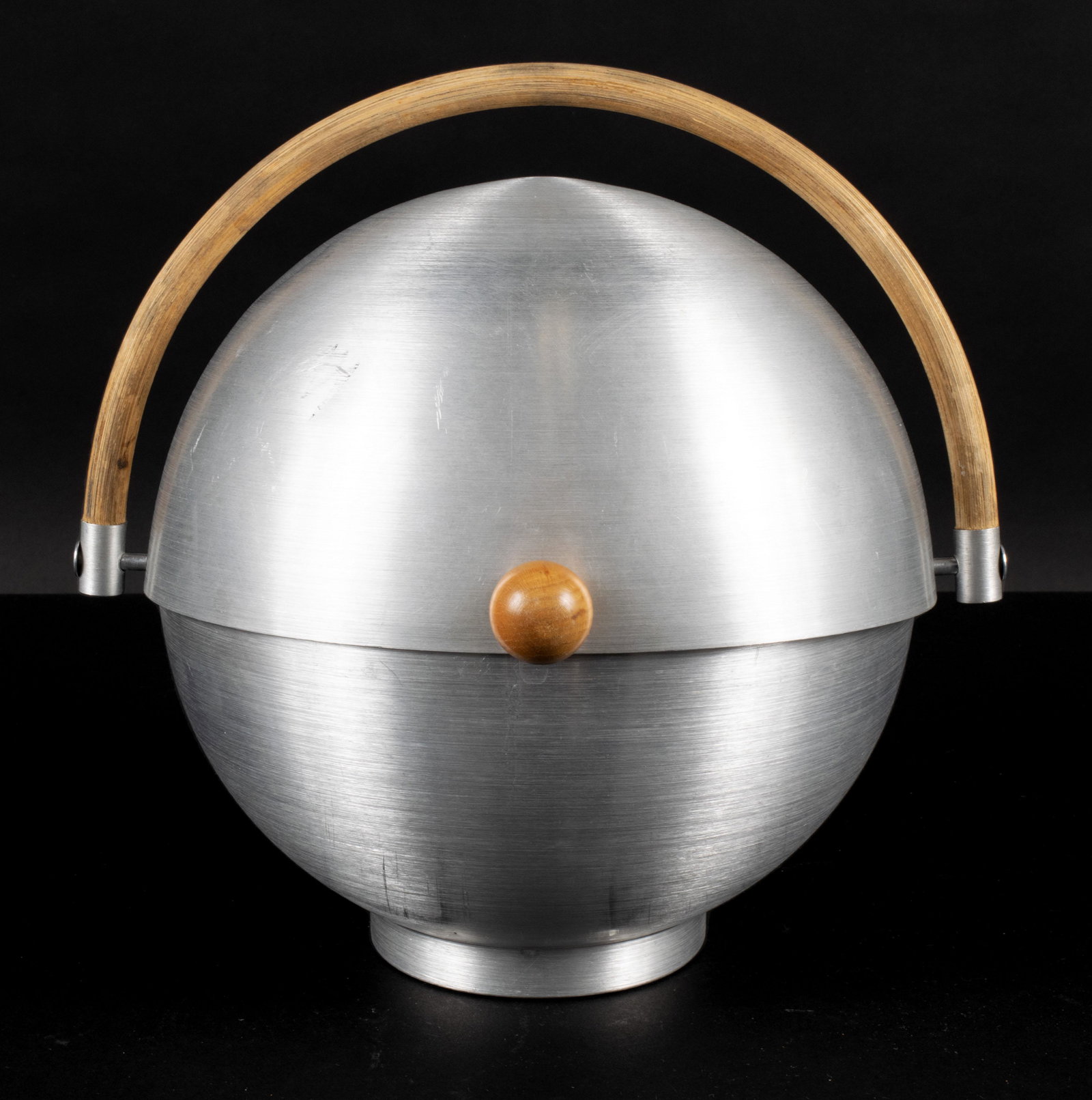 ART DECO RUSSEL WRIGHT MCM BUN WARMER: ART DECO RUSSEL WRIGHT MCM BUN WARMERAmerican, 1930s, aluminum, signed. Full sphere with circular footing, wooden knob handle to the sliding lid and full bentwood handle.8 1/4 in. (21 cm.)