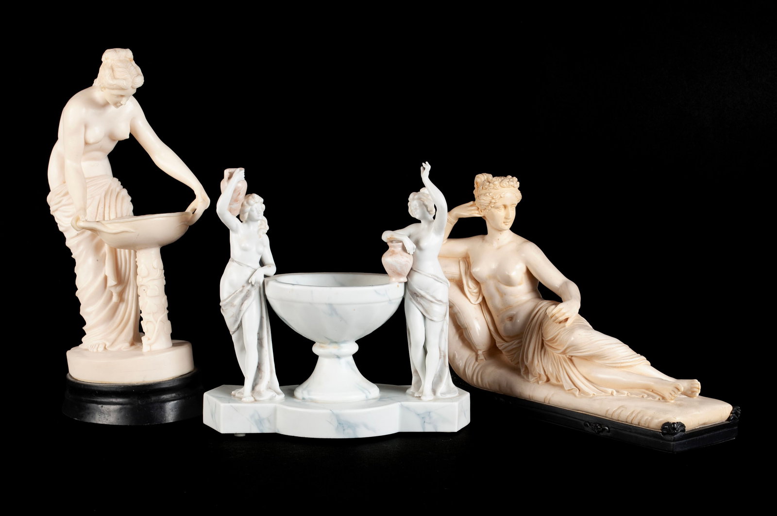 THREE CLASSICAL STYLE DECORATIVE FIGURES: THREE CLASSICAL STYLE DECORATIVE FIGURES20th century. Including a composition figure of a semi-nude woman leaning over a font, another composition figure of a semi-nude woman lying on a chaise, and a