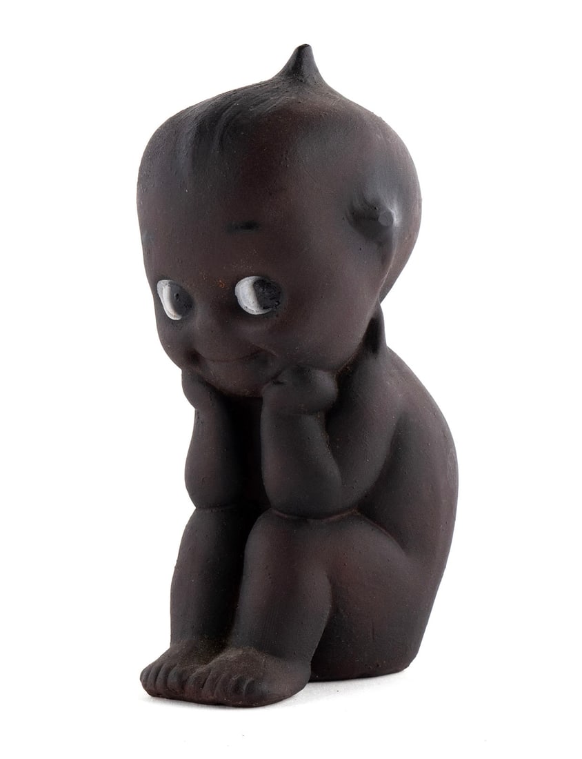 AFRICAN AMERICAN BISQUE KEWPIE THINKER: AFRICAN AMERICAN BISQUE KEWPIE THINKERGerman, early 20th century. Seated child with chin resting on hand and a side eye glance. Marked Rose O?Neill Kewpie Germany.4 1/4 x 1 3/4 x 2 1/2 in. (10.8 x 4.4