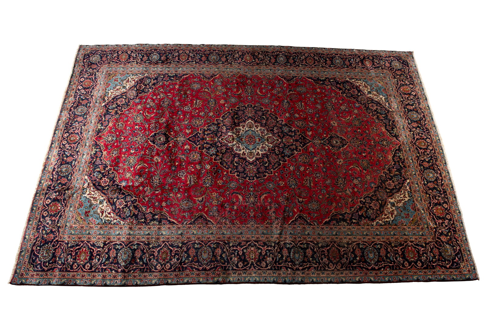KASHAN ROOM RUG: KASHAN ROOM RUG Persian, 20th century. Blue on ivory on navy foliate pole medallion centers the floral decorated red field with corners matching the medallion, navy border with multiple guard borders.