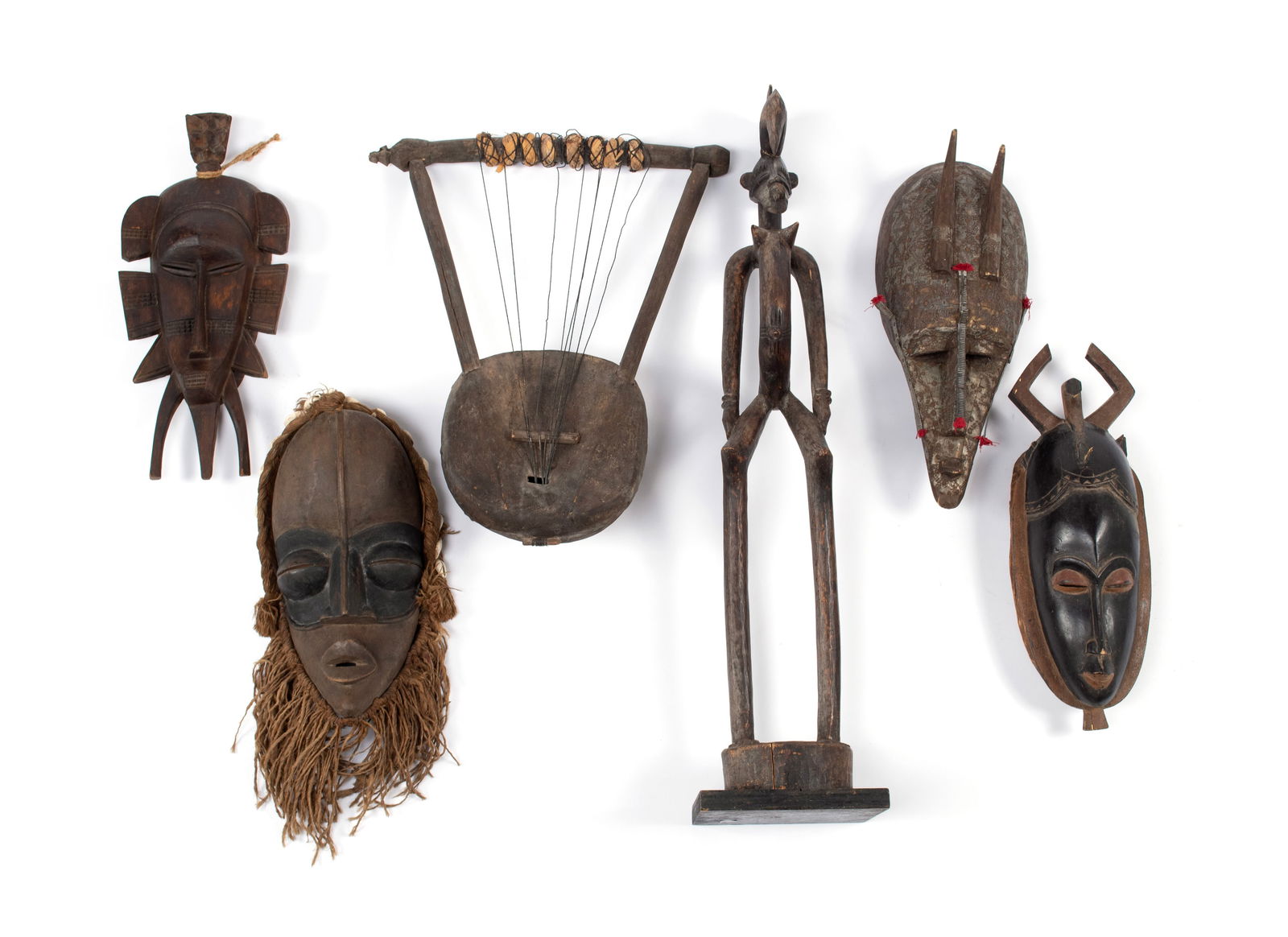 SIX AFRICAN TRIBAL CARVINGS: SIX AFRICAN TRIBAL CARVINGS20th century. Kpelie mask, Dan mask, Marka mask, a Baule or Yaure mask, Ugandan or Kenyan Lyre (harp), and a Senufo altar figure.Largest: 30 3/4 x 7 x 7 in. (78.1 x 17.8 x 1