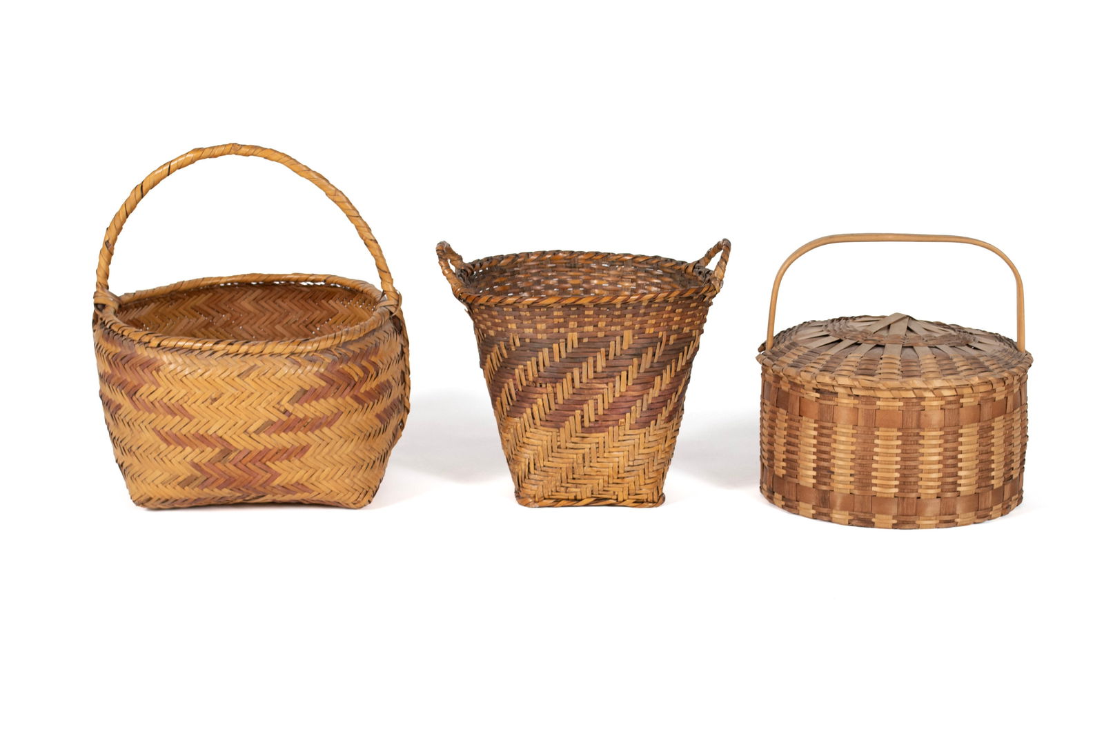 THREE NATIVE AMERICAN BASKETS: THREE NATIVE AMERICAN BASKETS20th century. Choctaw River single handle cane basket, Choctaw River double-handled cane basket and an Eastern Woodlands lidded single handle splint feather basket.Feather
