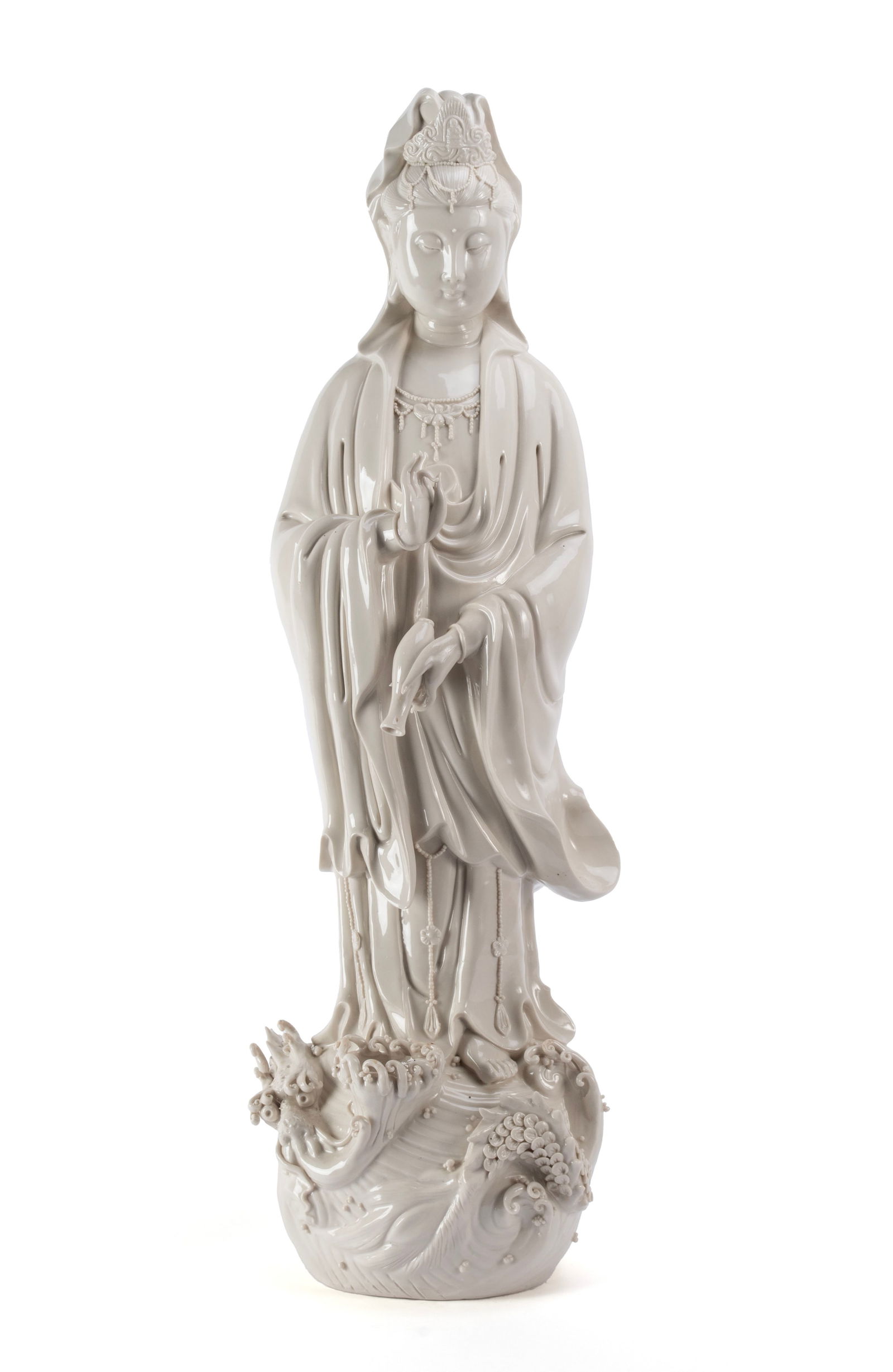 BLANC DE CHINE QUAN YIN: BLANC DE CHINE QUAN YINChinese, 20th century. Depicts a standing Quan Yin, holding a vase upside down in her hand, on a scroll decorated pedestal below.29 1/2 x 9 in. (74.9 x 22.9 cm.)