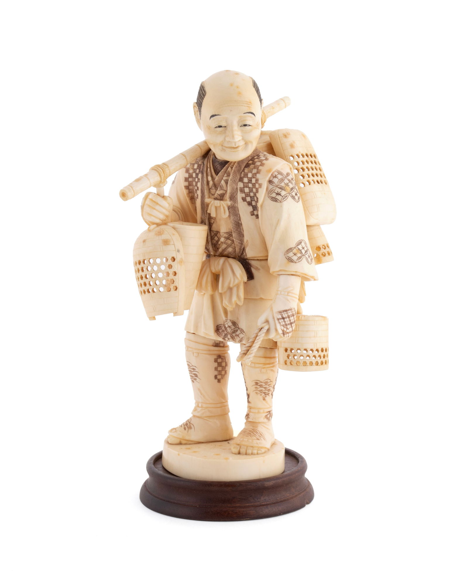 CARVED OKIMONO OF A MERCHANT: CARVED OKIMONO OF A MERCHANT Japanese,19th/early 20th century. Full-bodied figure of a basket seller, bamboo balanced across his shoulder with numerous baskets attached, an intricate incised pattern