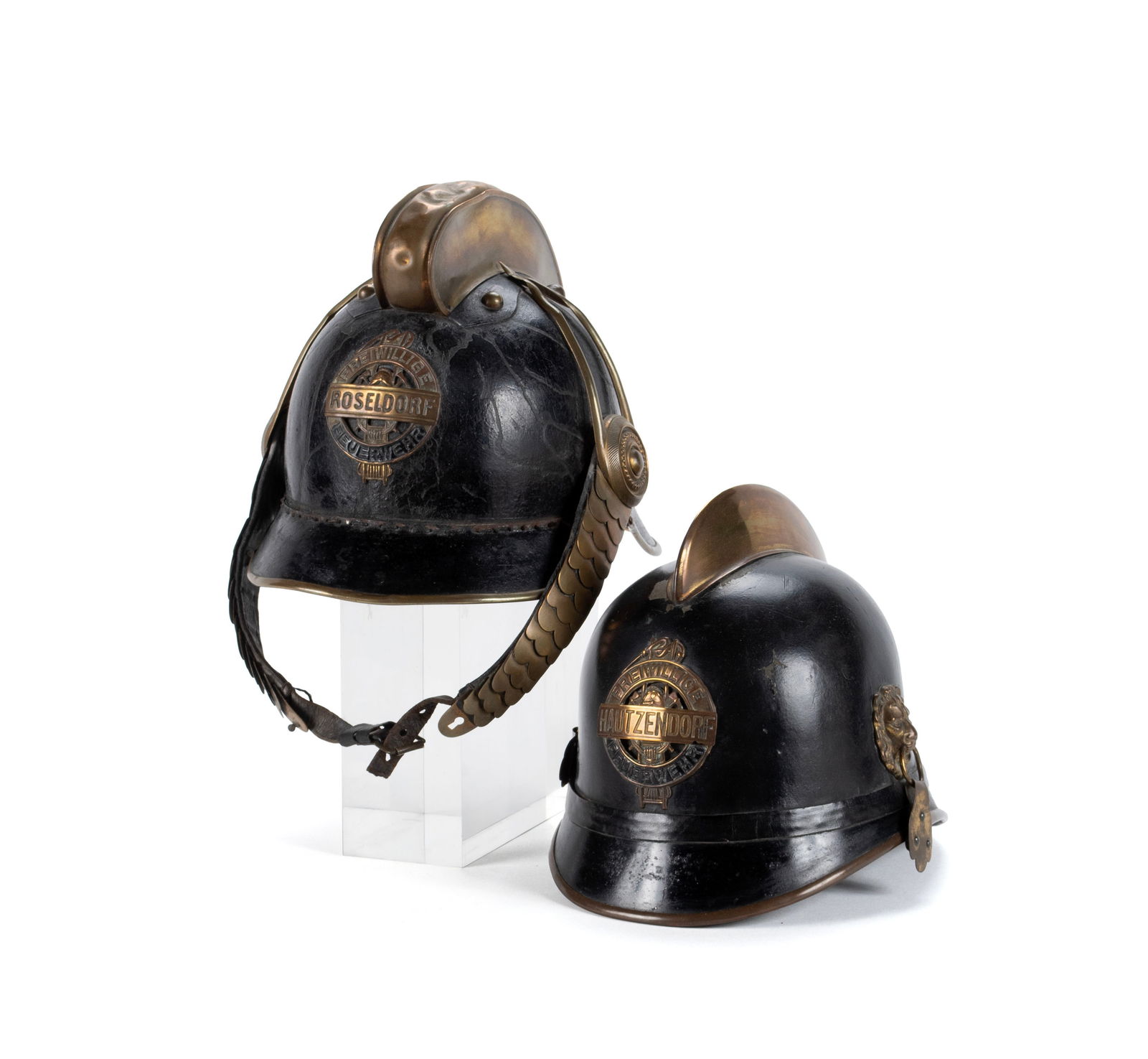 TWO GERMAN FIREFIGHTER HELMETS: TWO GERMAN FIREFIGHTER HELMETS German, circa 1900. Both of black leather, one with a "ROSELDORF" badge to the front, the other with a "HAUTZENDORF" badge, one manufactured by Josef Zimbler, the other